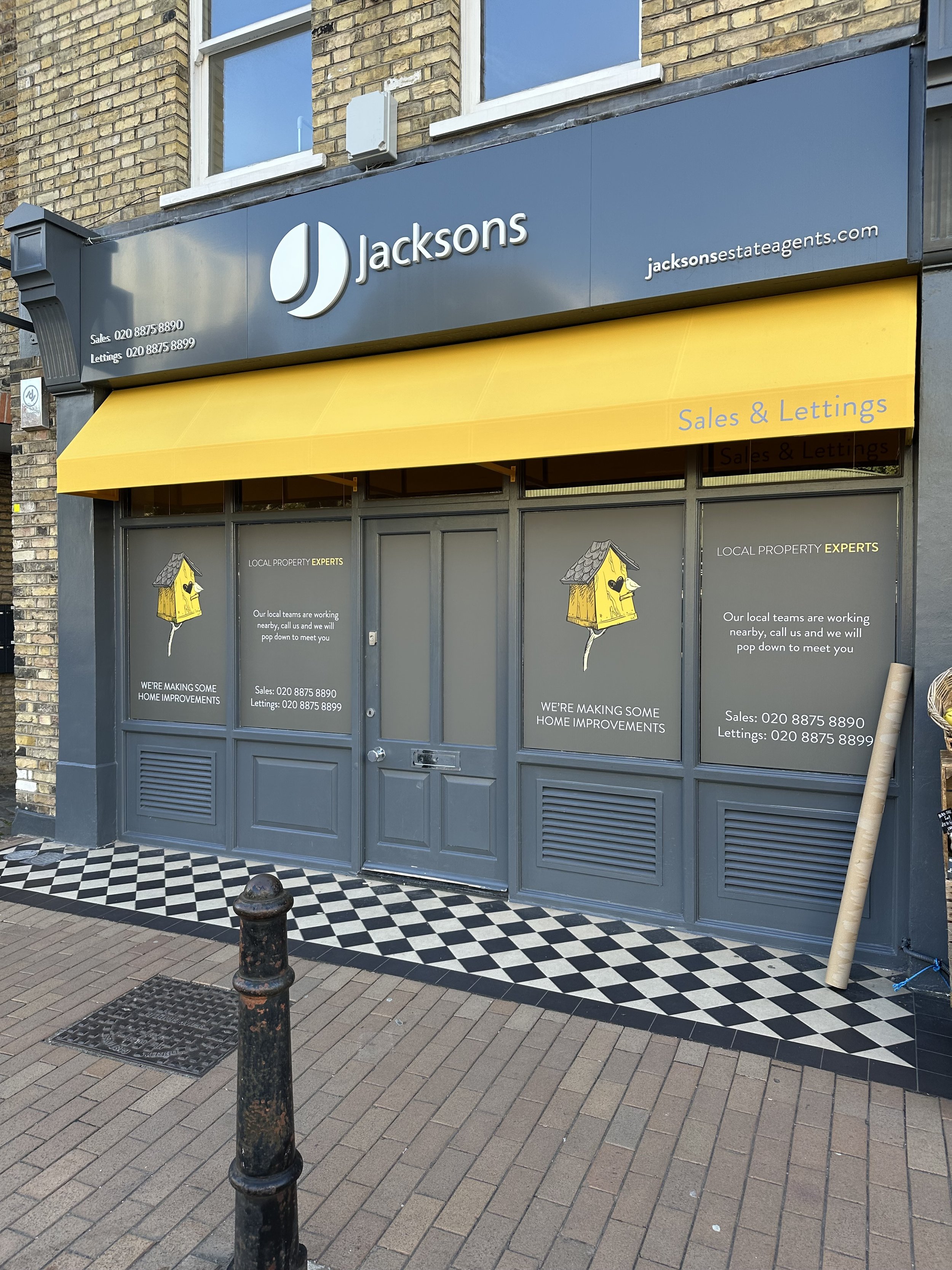 Storefront of Jacksons estate agents with a gray and yellow sign, with window graphics fitted