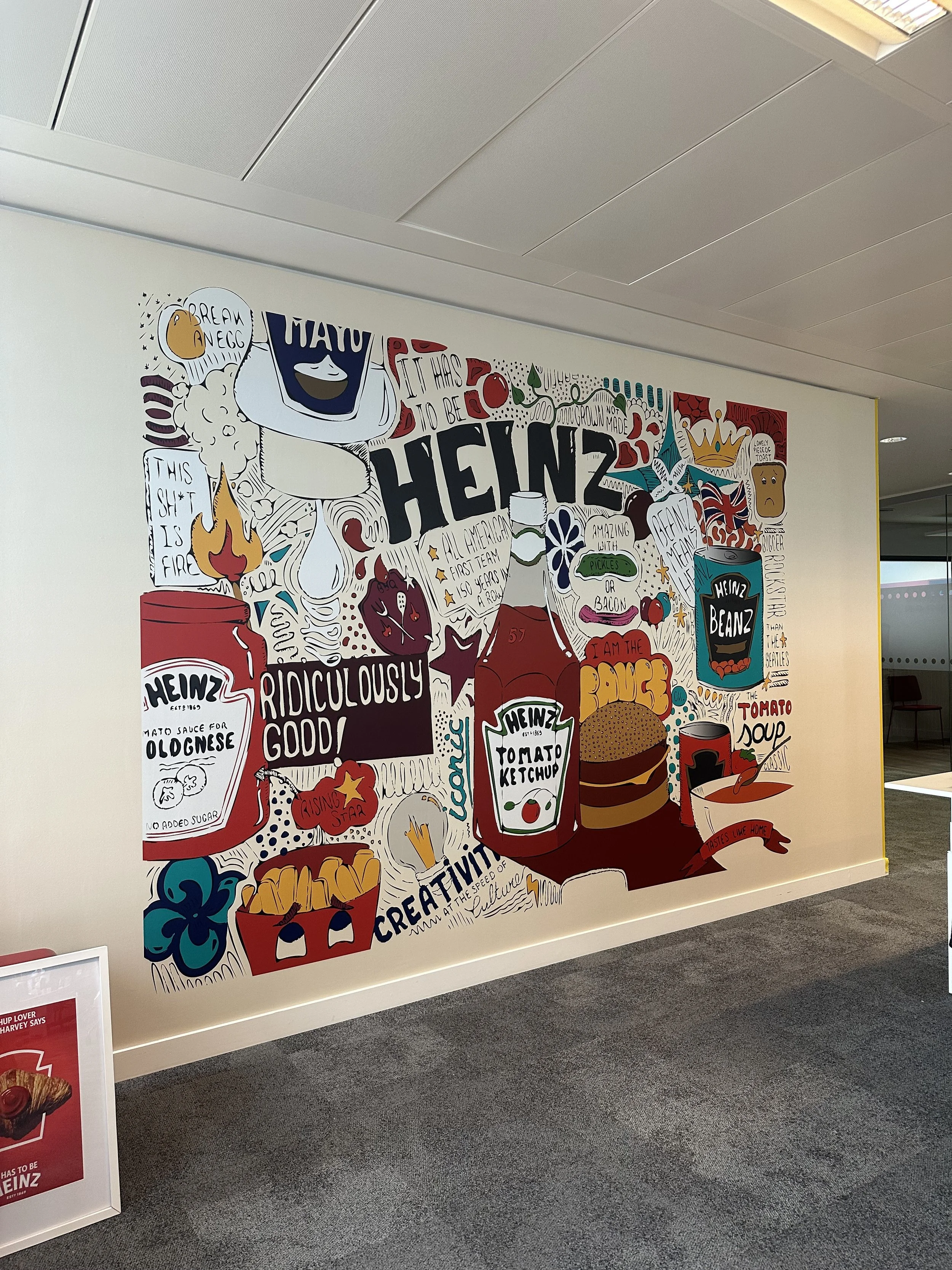 Colorful one piece wall paper with wall mural depicting various Heinz products and related illustrations, with handwritten-style text and artistic designs, located in the shard