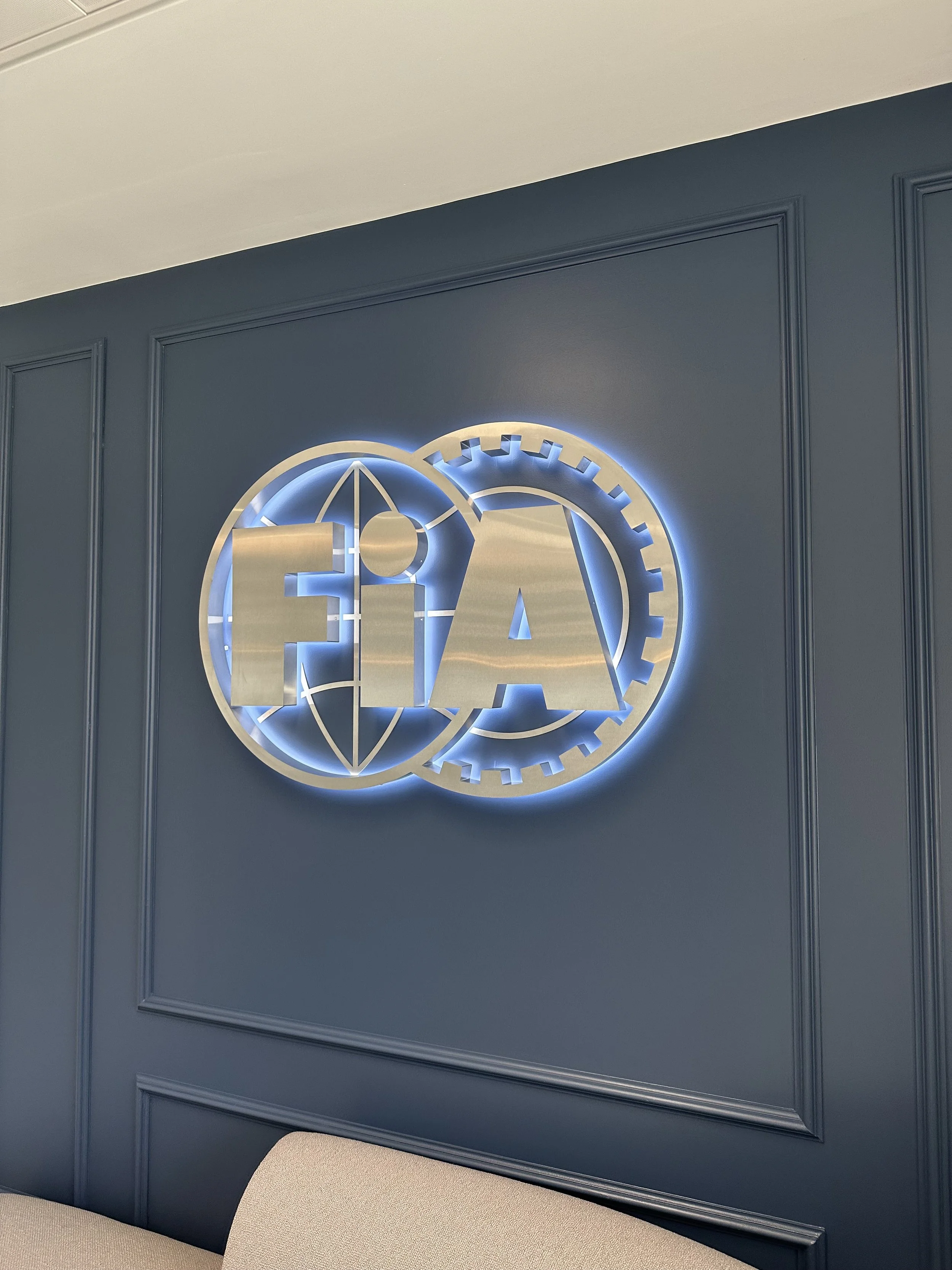 Decorative wall with a metallic logo featuring a globe and gears, illuminated with a backlight, mounted on a blue paneled wall in an office or conference room