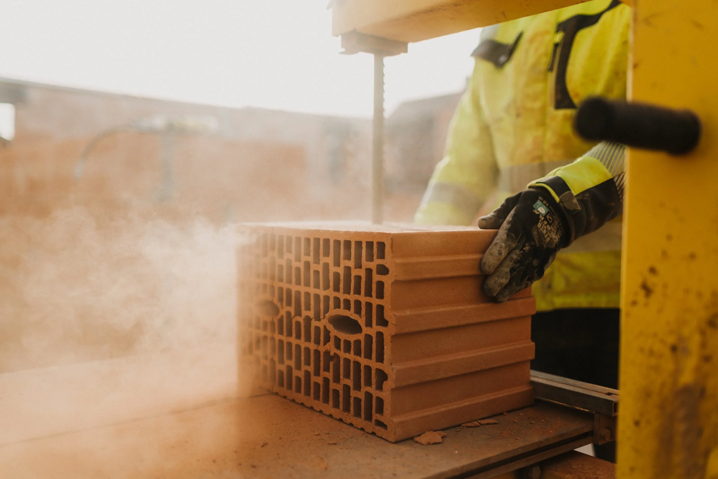 Handwerker legt Ziegelstein in eine Bauplatte, während Staub aufwirbelt.