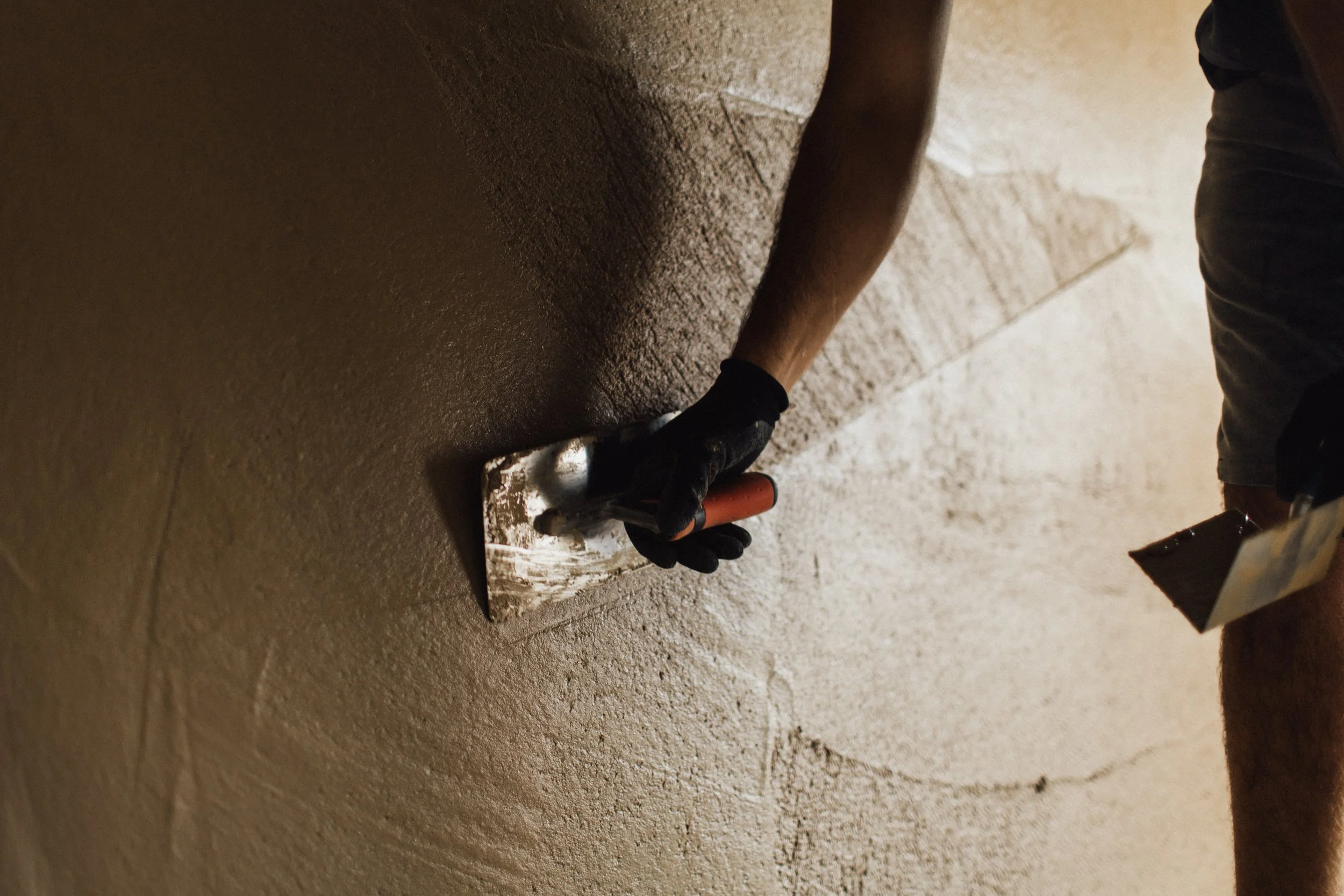 Hand eines Arbeiters, der einen Pinsel benutzt, um eine Wand zu verputzen.