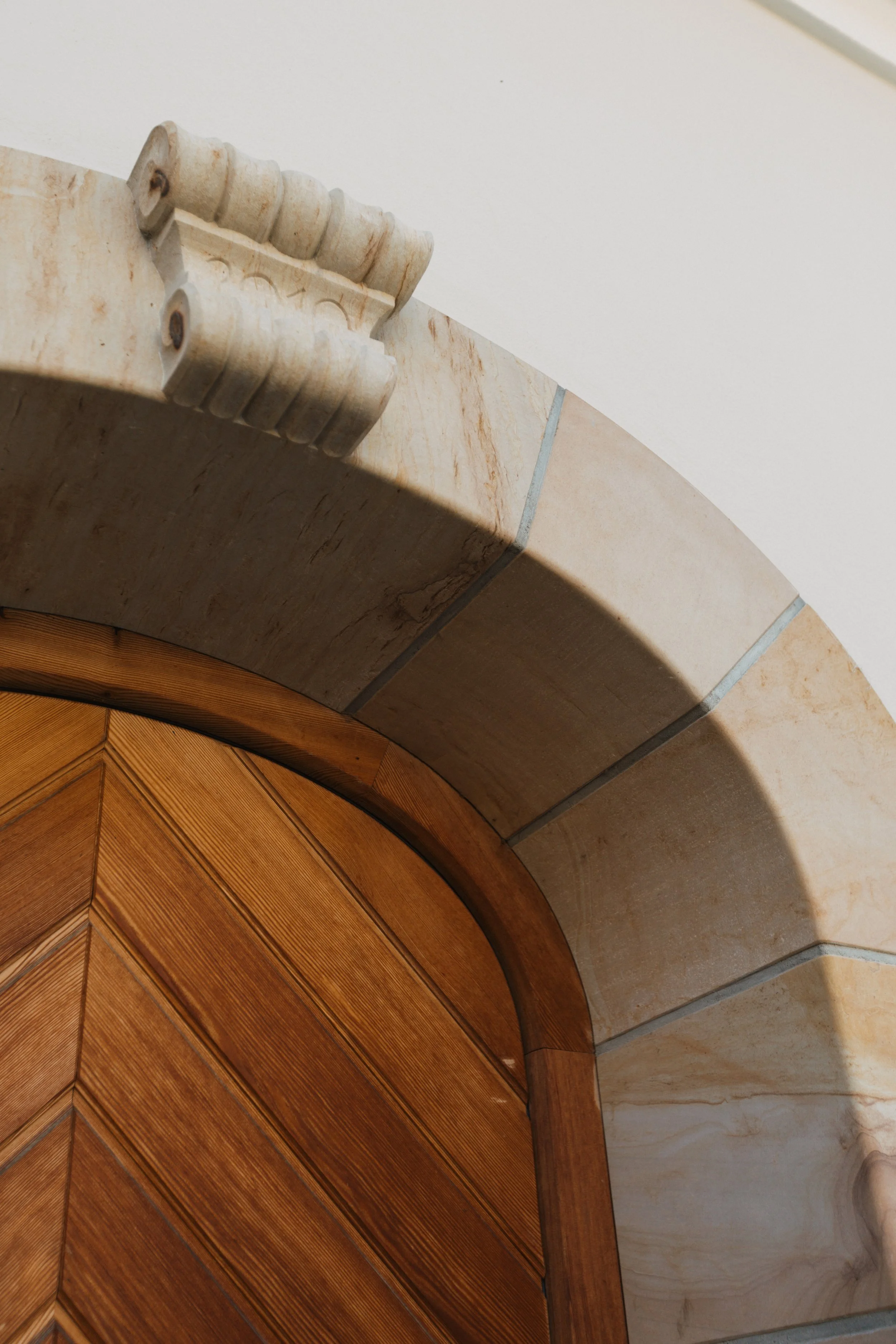 Ein Blick auf einen Bördelbogen, der aus Marmor besteht, und einen Holzrahmen mit schrägen Linien sowie einen Schatten auf einer weißen Wand.