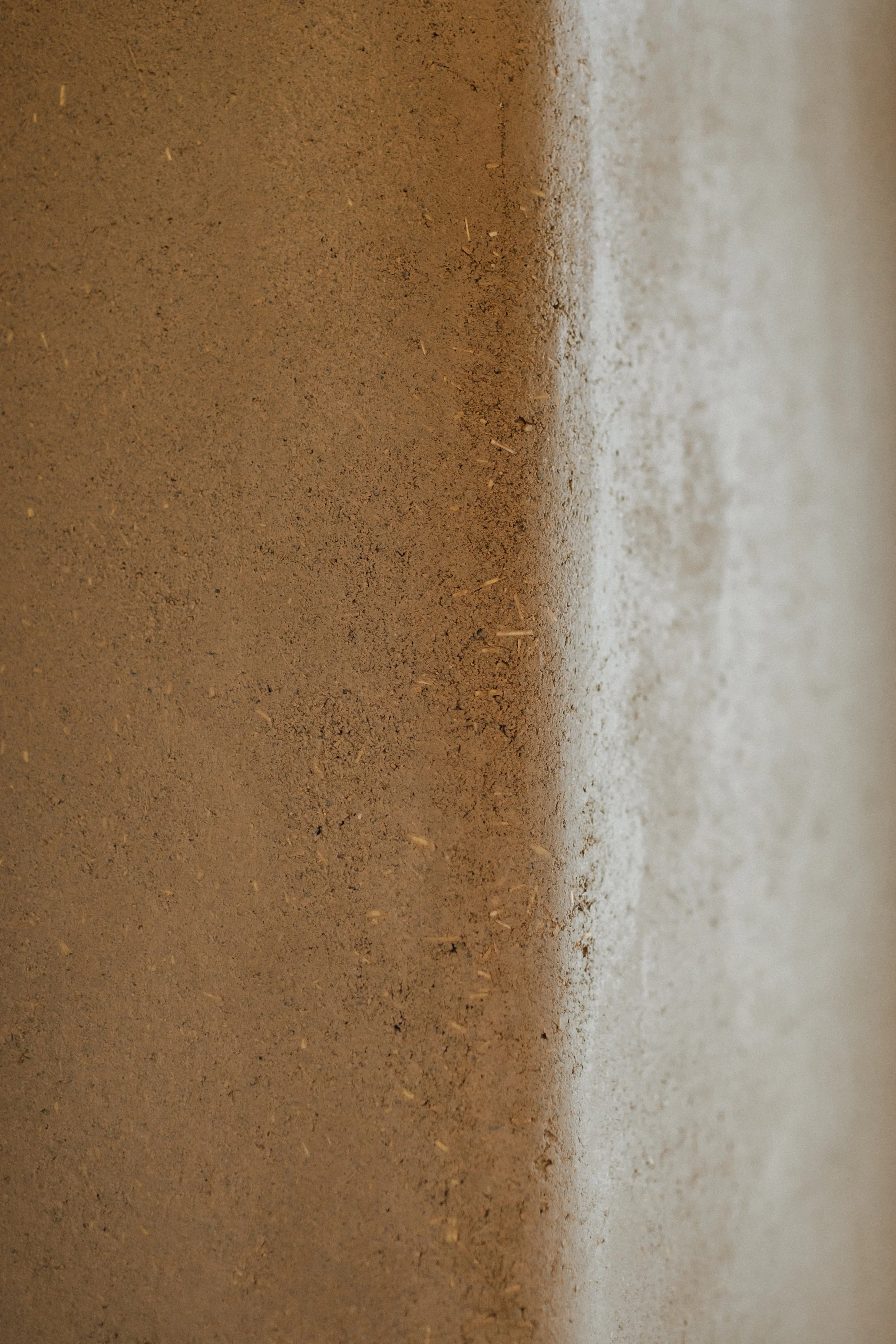 Nahaufnahme einer Wand mit rauer, sandiger Oberfläche in braunen und hellen Tönen.