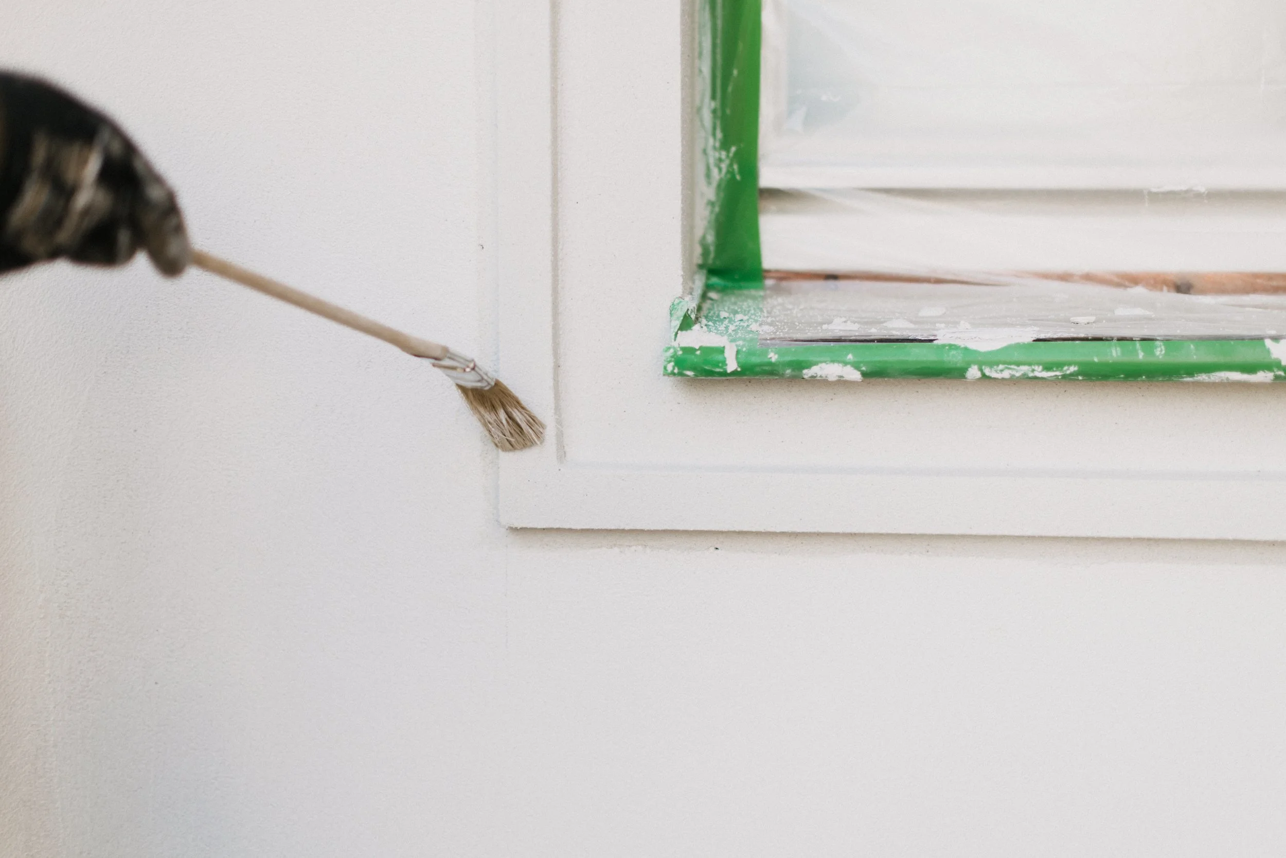 Hand mit Pinsel, die eine Wand streicht, neben einem Fensterrahmen