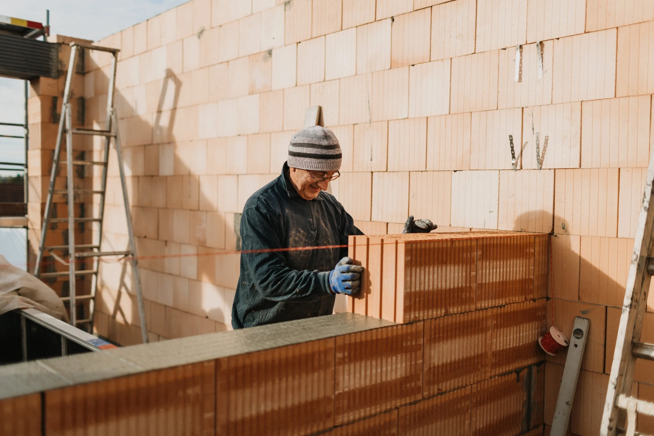 Ein Mann beim Mauerbau befestigt Ziegelsteine an einer Hauswand im Bau.