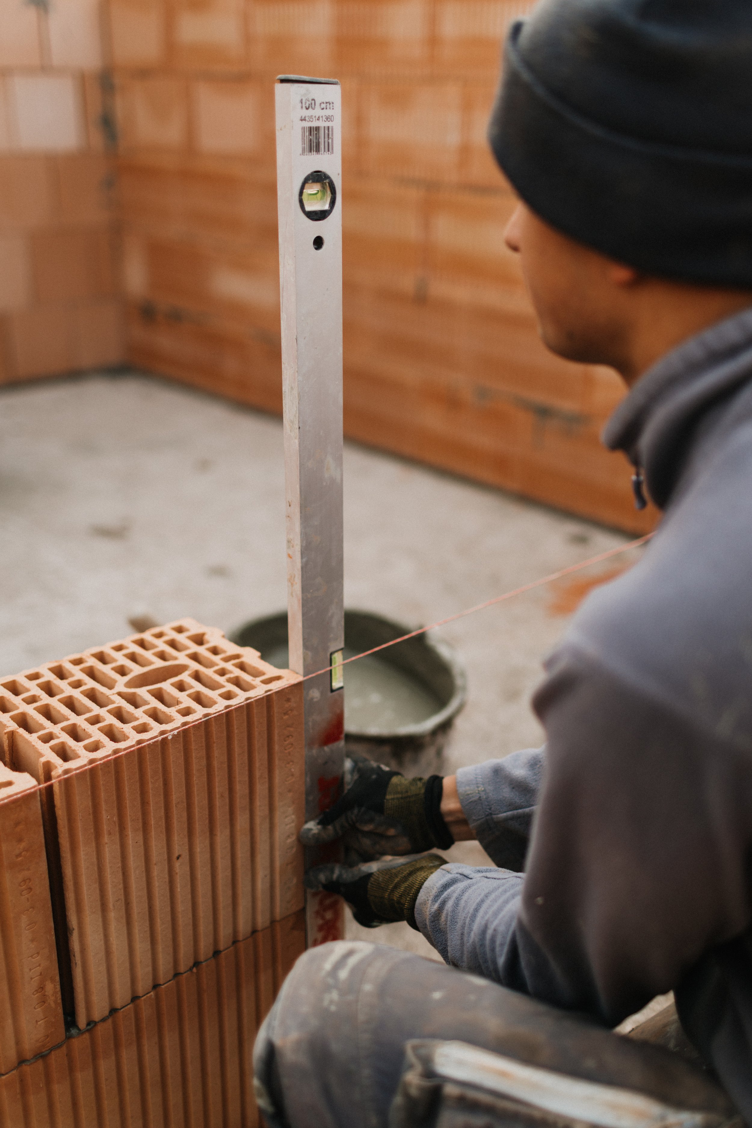 Ein Bauarbeiter legt Ziegelsteine auf eine Mauer, während er eine Wasserwaage zur Ausrichtung benutzt.