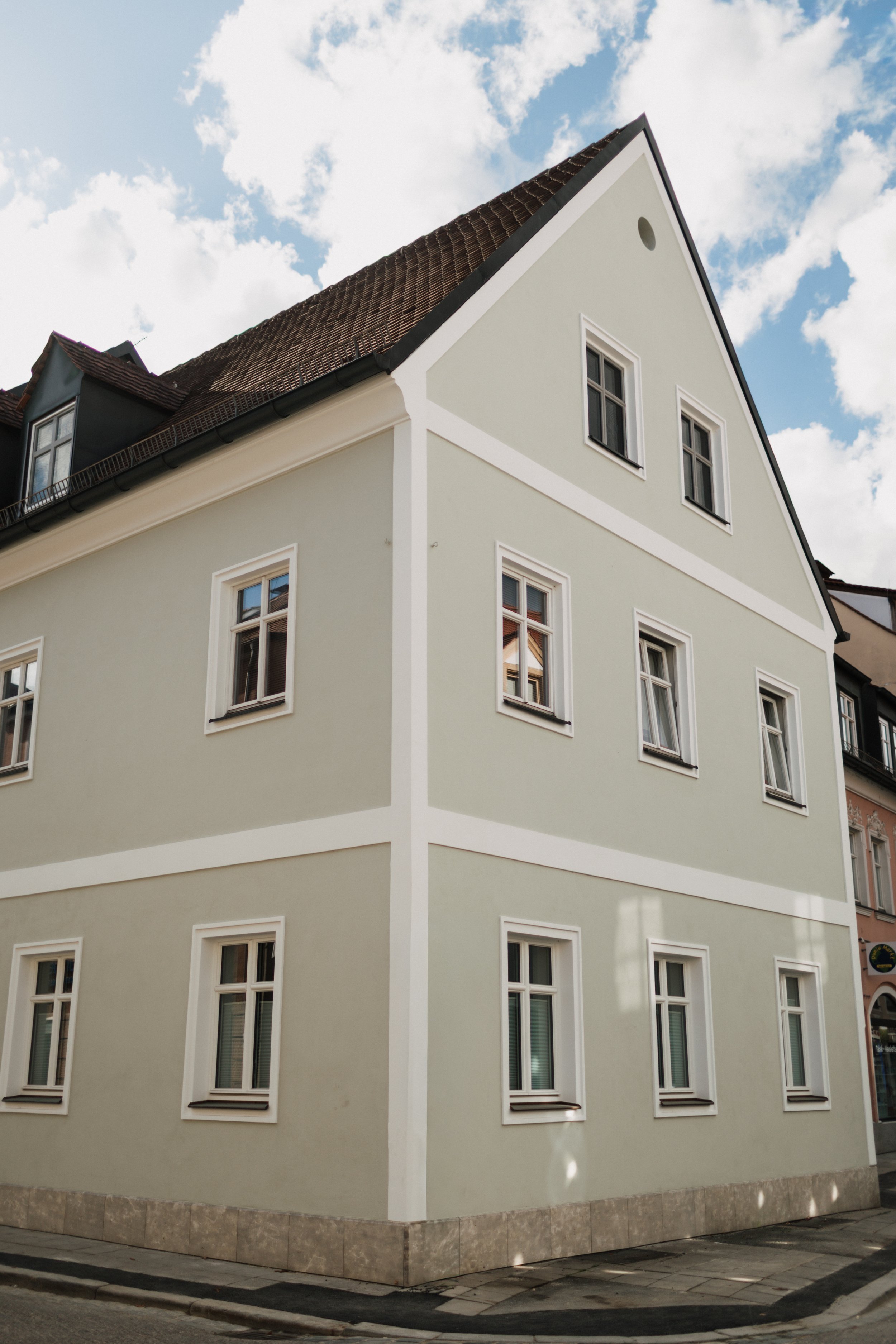 Mehrstöckiges Haus mit weißem Rahmen und neun Fenstern, grüner Fassade, geneigtem Dach, voller blauer Himmel mit Wolken.