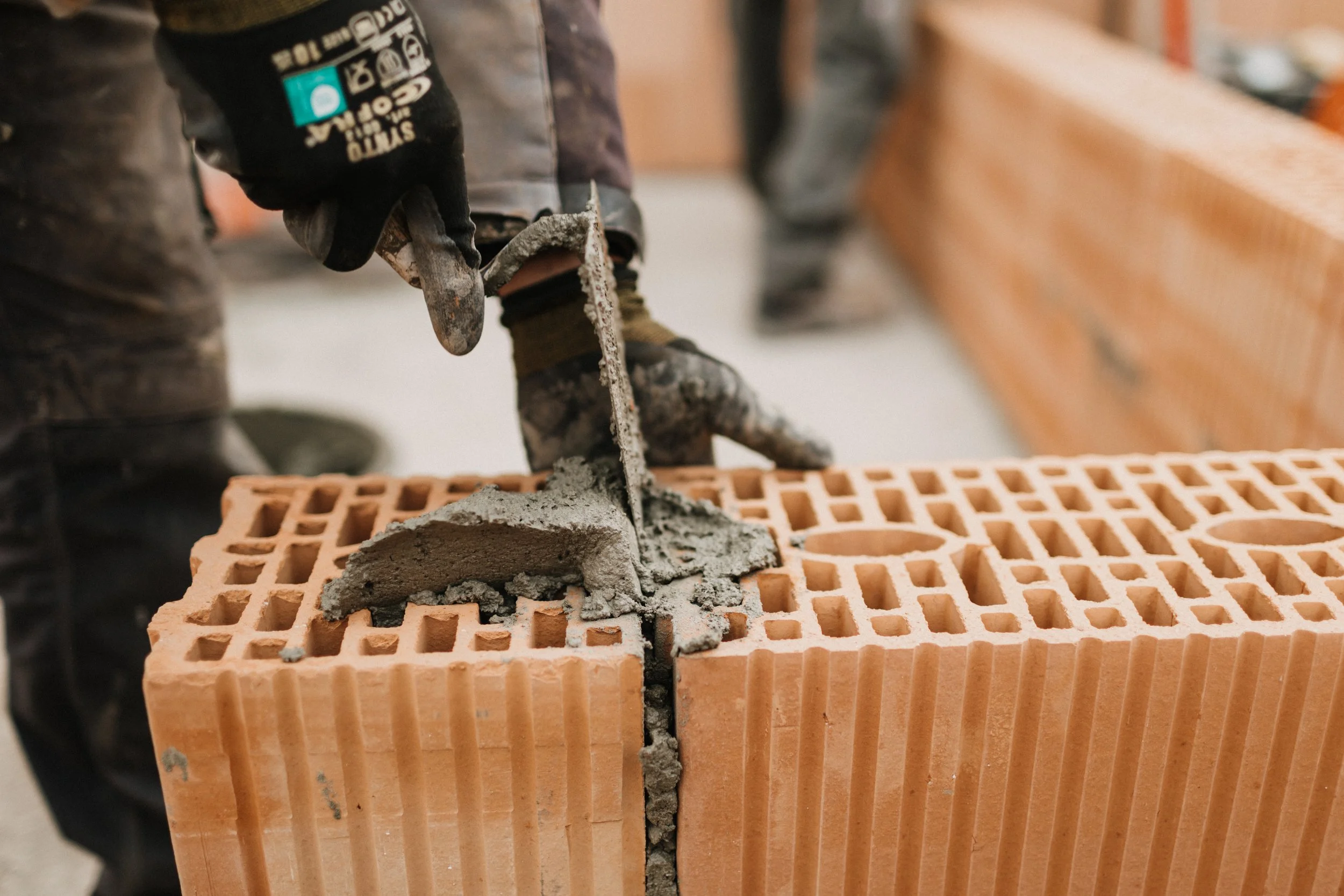 Mitarbeiter legt Mörtel auf einen Ziegelstein bei einer Baustelle.
