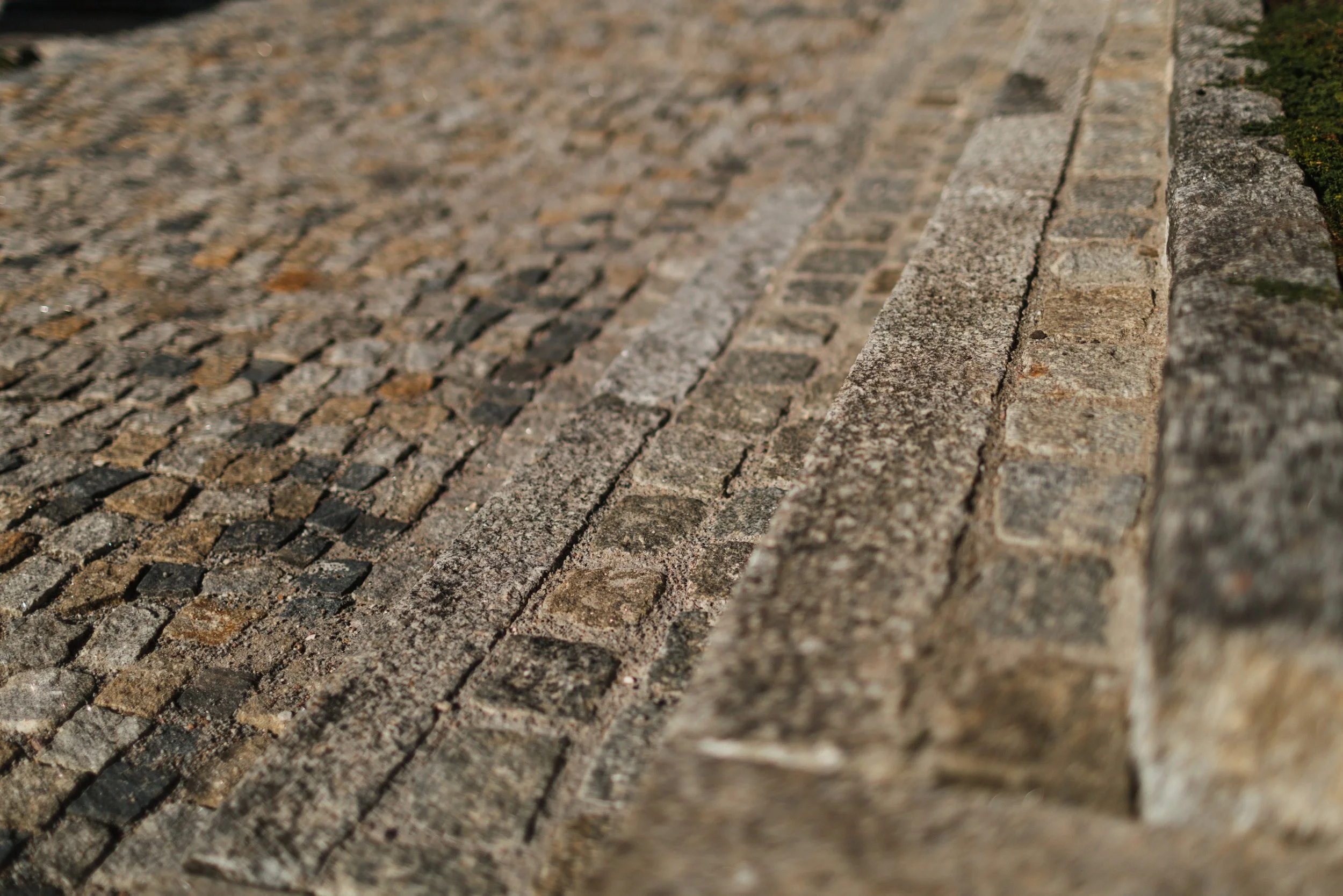 Blick auf eine gepflasterte Bürgersteigkante, bestehend aus verschiedenen Steinen und Zement