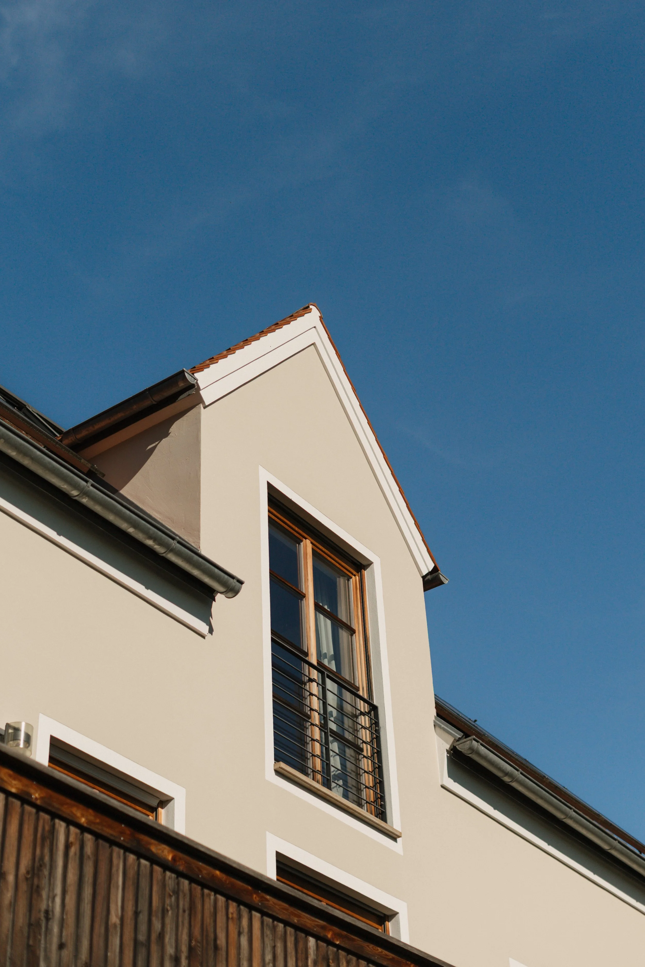 Ein modernes Haus mit einer großen Fensterkuppel und Sichtschutzgeländer, unter blauem Himmel.