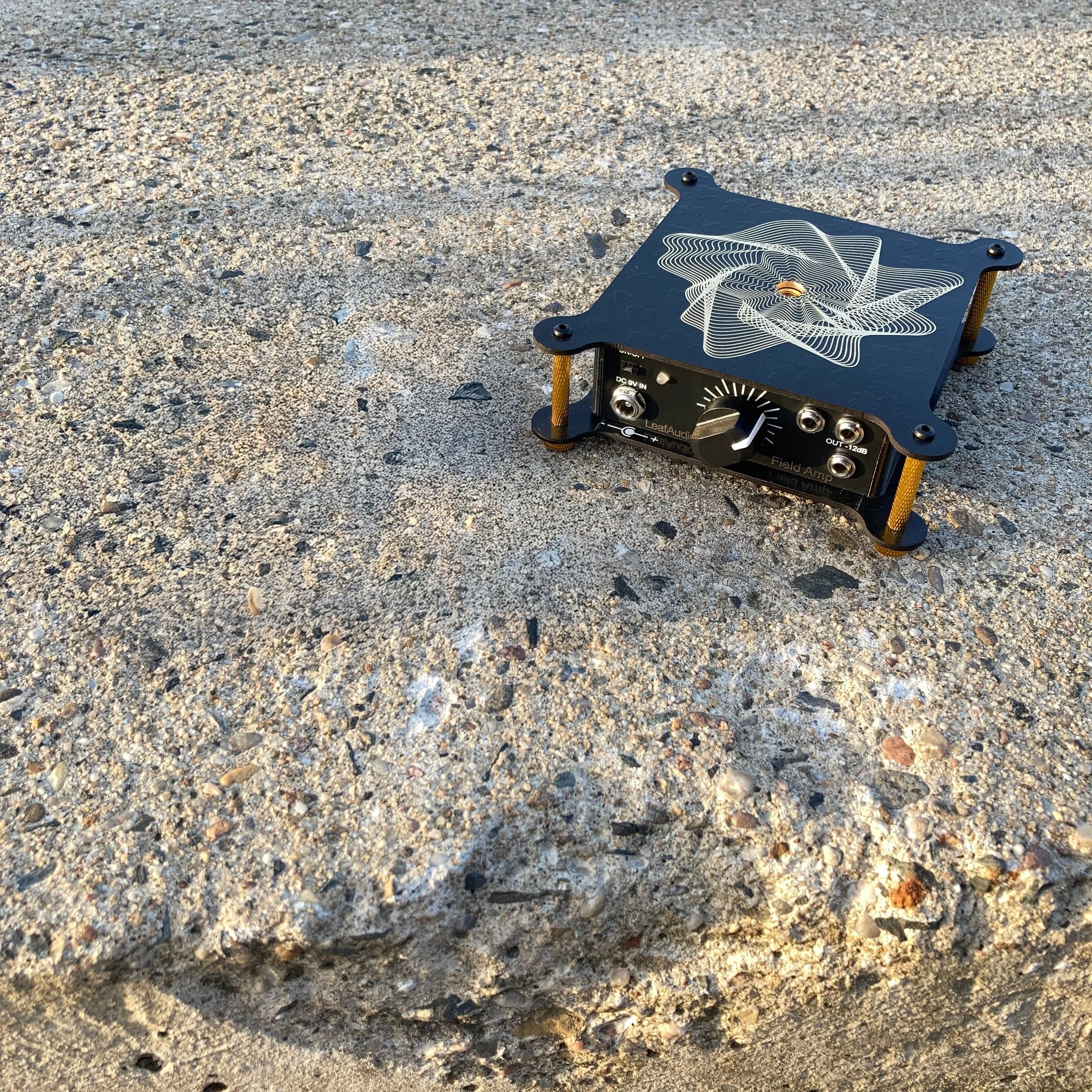 A small black electronic device with a decorative top, placed on a sandy surface.