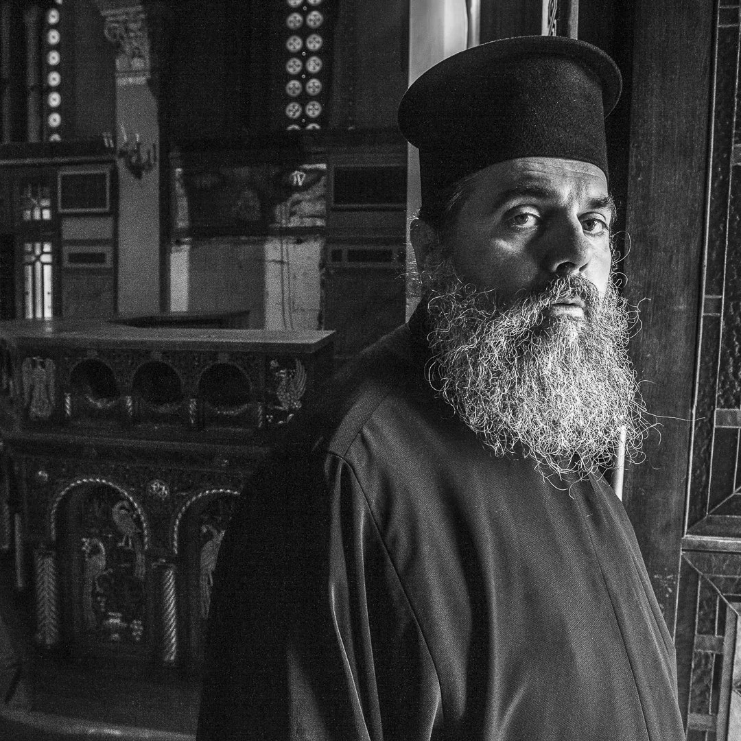 En prest står i døråpningen til kirken sin i Athen