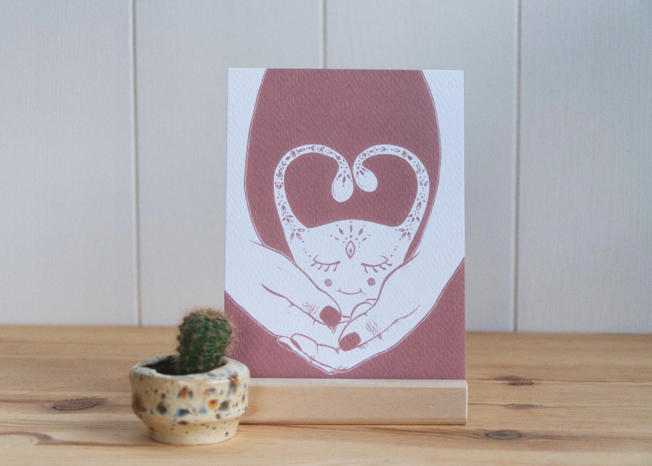 Eine Postkarte welche einen aufwändig geschmückten und glücklich entspannten Uterus zeigt, welcher Liebevoll von zwei Händen gehalten wird