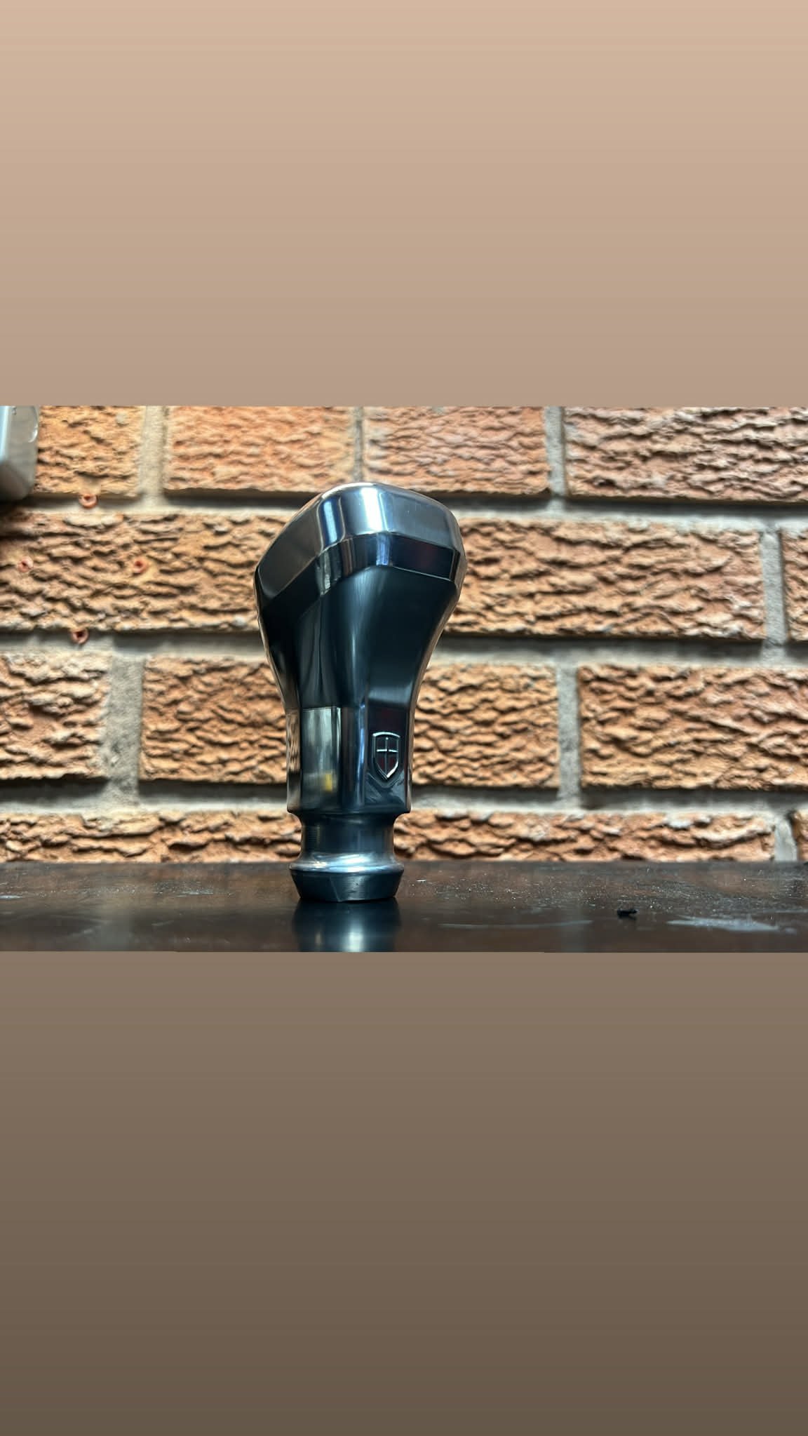 A black and silver gear shifter placed on a wooden surface in front of a brick wall.