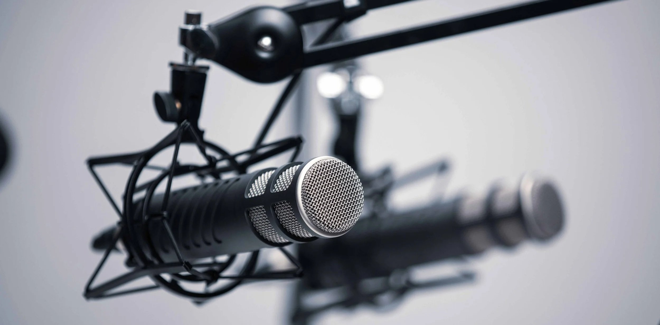 Close-up of a professional microphone mounted on a stand, with a pop filter, on a gray background, suitable for podcasting or broadcasting.
