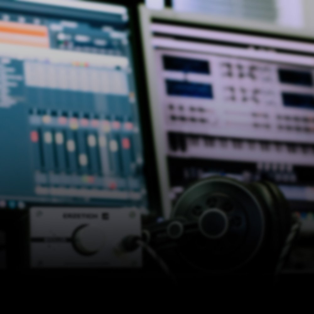 Blurred image of a music production setup with a computer screen displaying a digital audio workstation, audio equipment, and headphones.