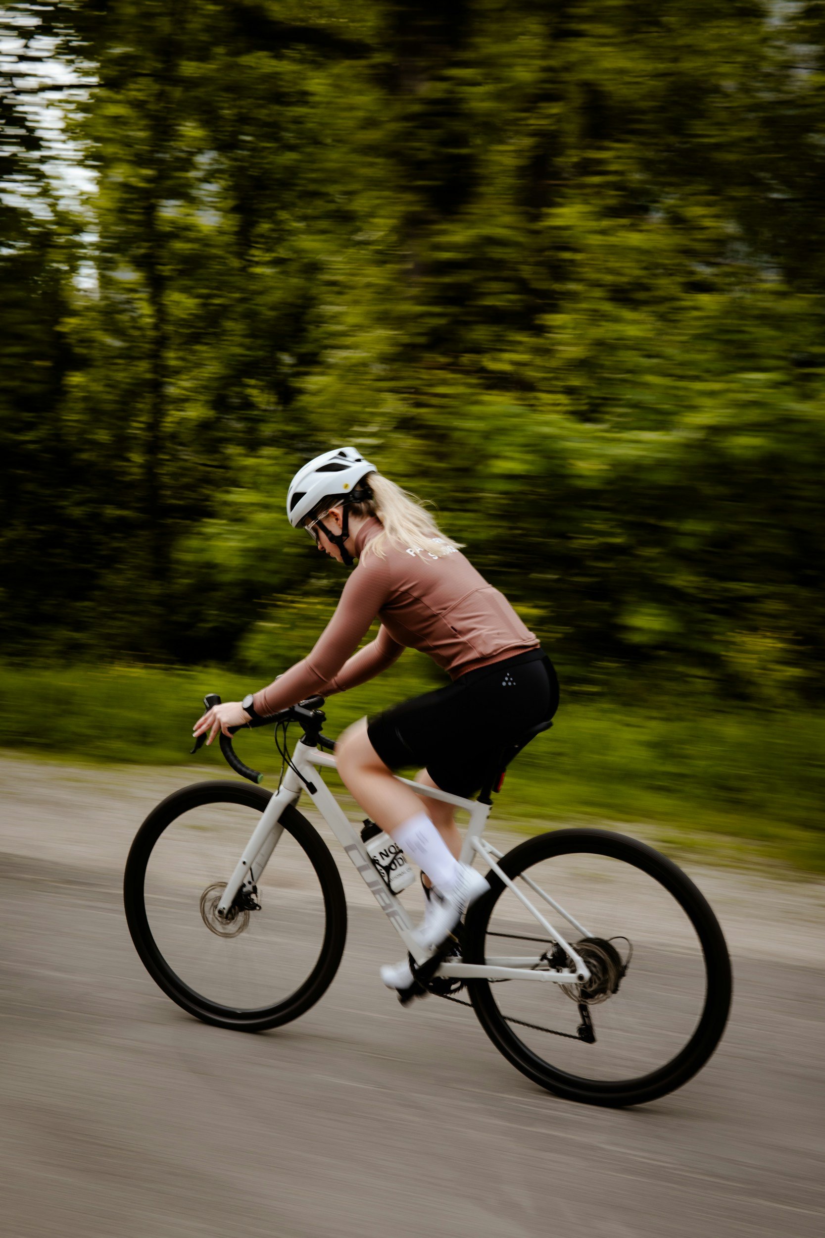 Person riding a mountain bike on a trail, wearing a helmet and sports attire, with blurred greenery in the background.