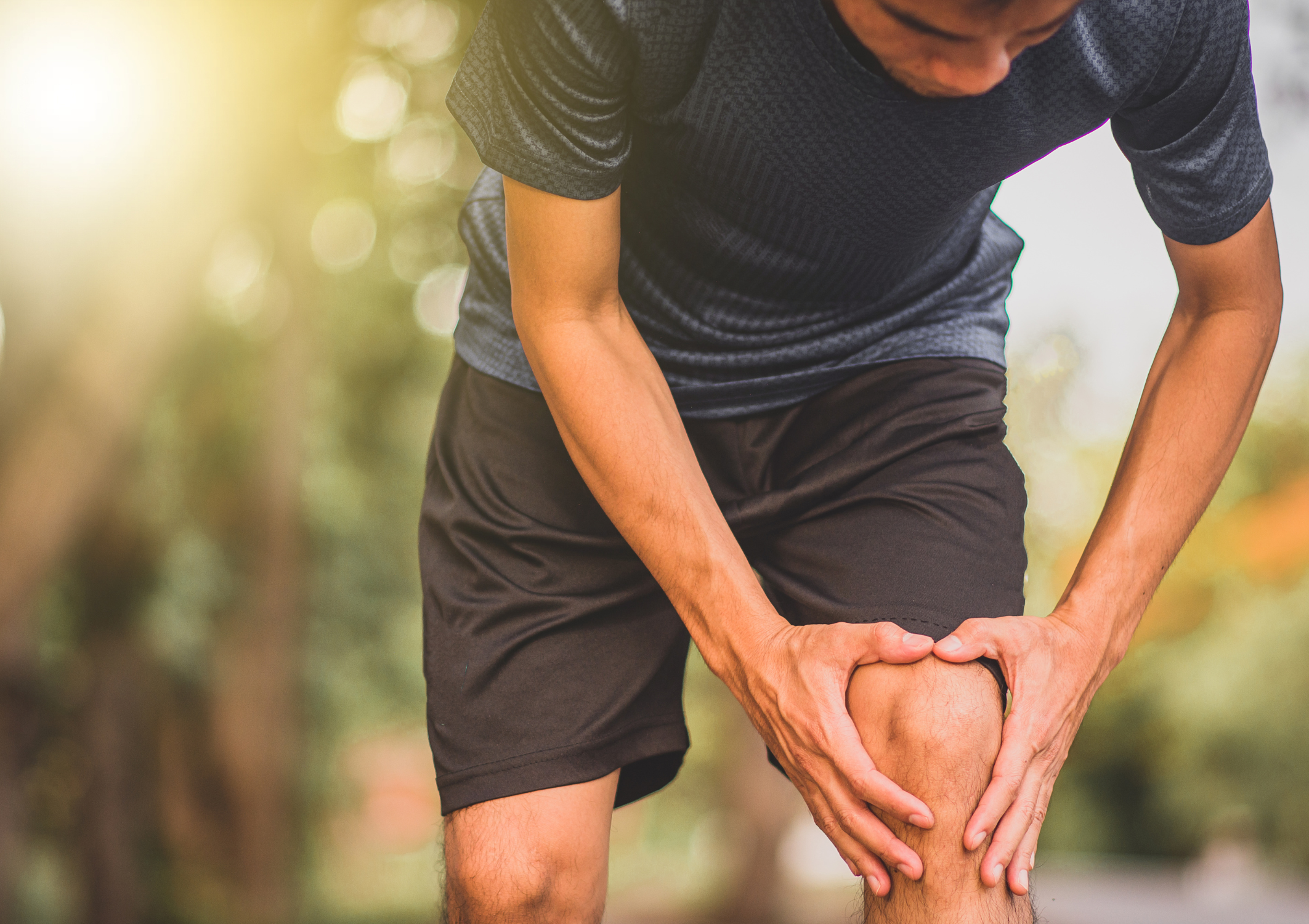 A man in activewear holding his knee in discomfort, illustrating joint pain and the need for bone density health checks.
