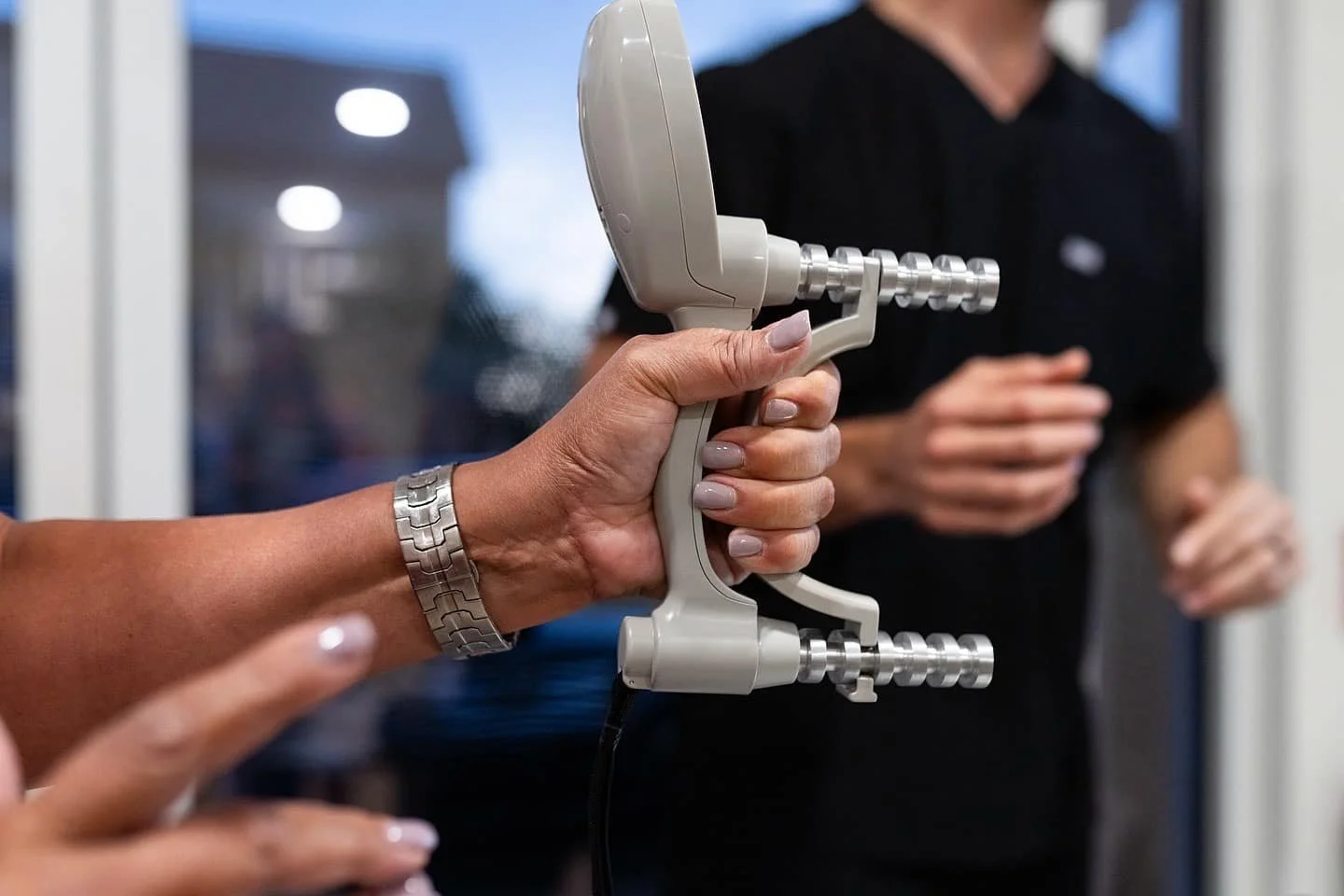 Person holding a medical device with multiple metallic prongs in front of another person in a dark shirt.