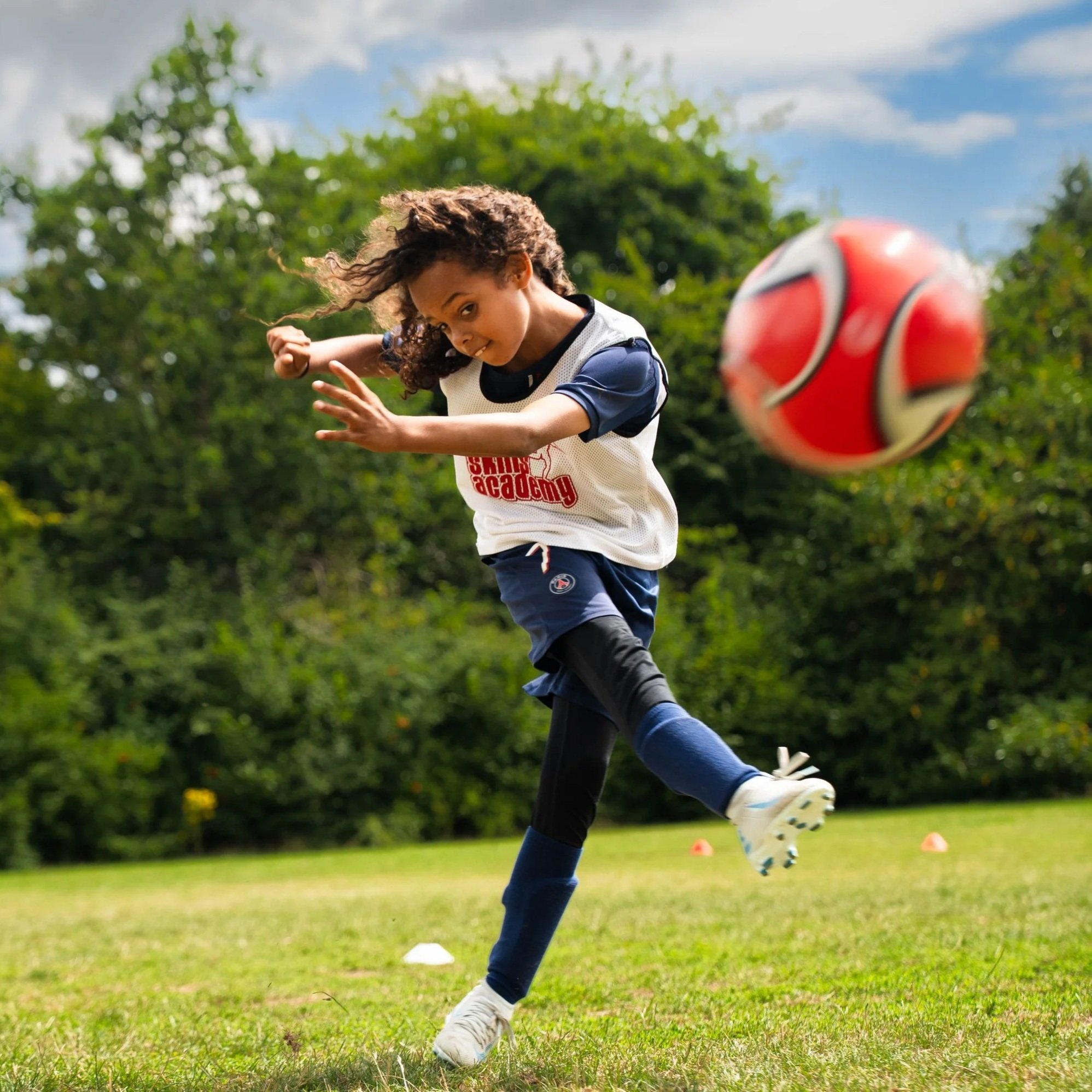 A kid wearing a skills academy bib and kicking a football