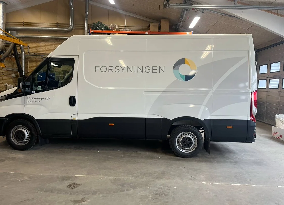 Side view of a white delivery van with the logo and text 'Forsyningen' on the side, parked inside a garage or warehouse.