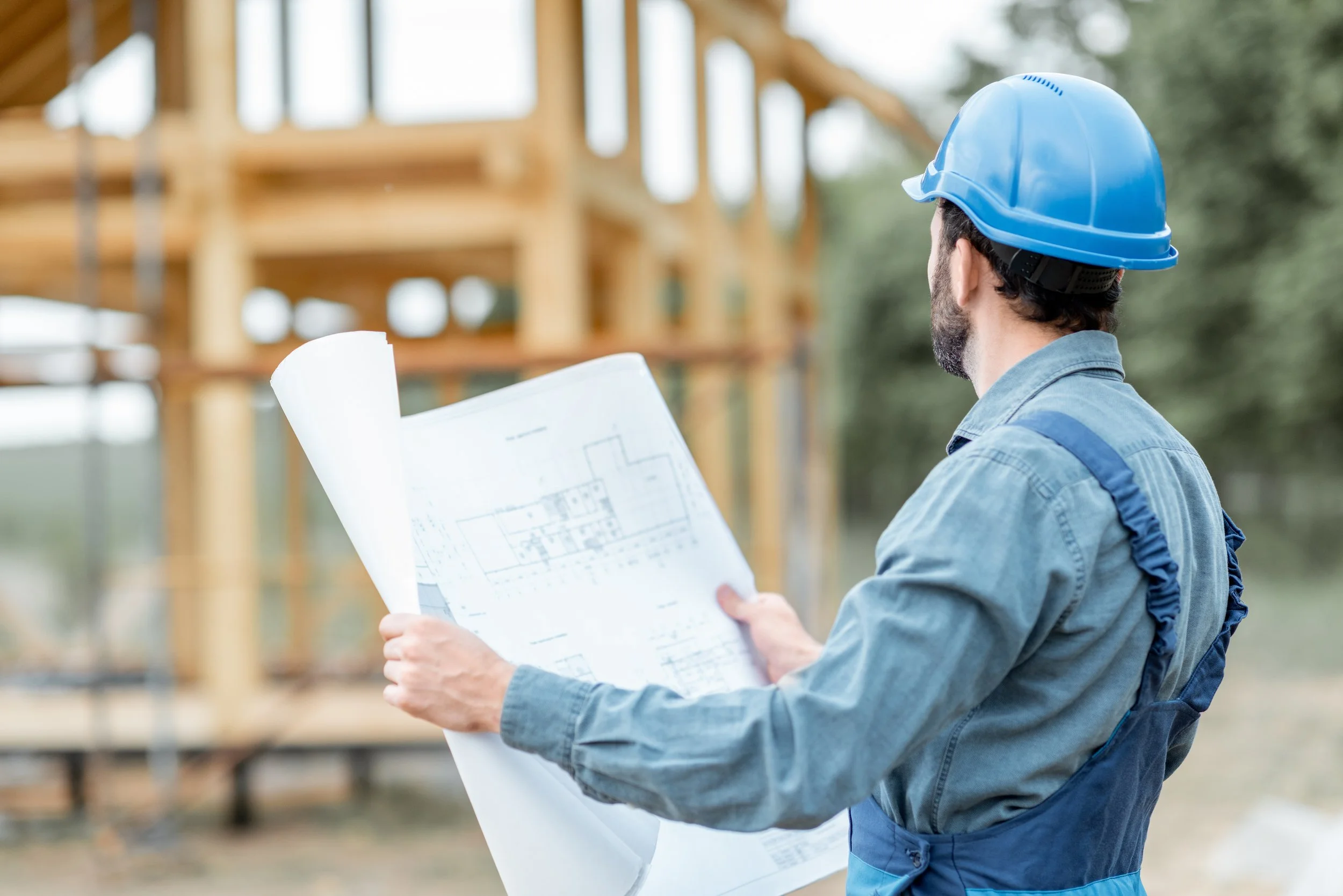 Ingénieur ou architecte portant un casque de sécurité regarde des plans de construction lors d'un site de bâtiment en bois.