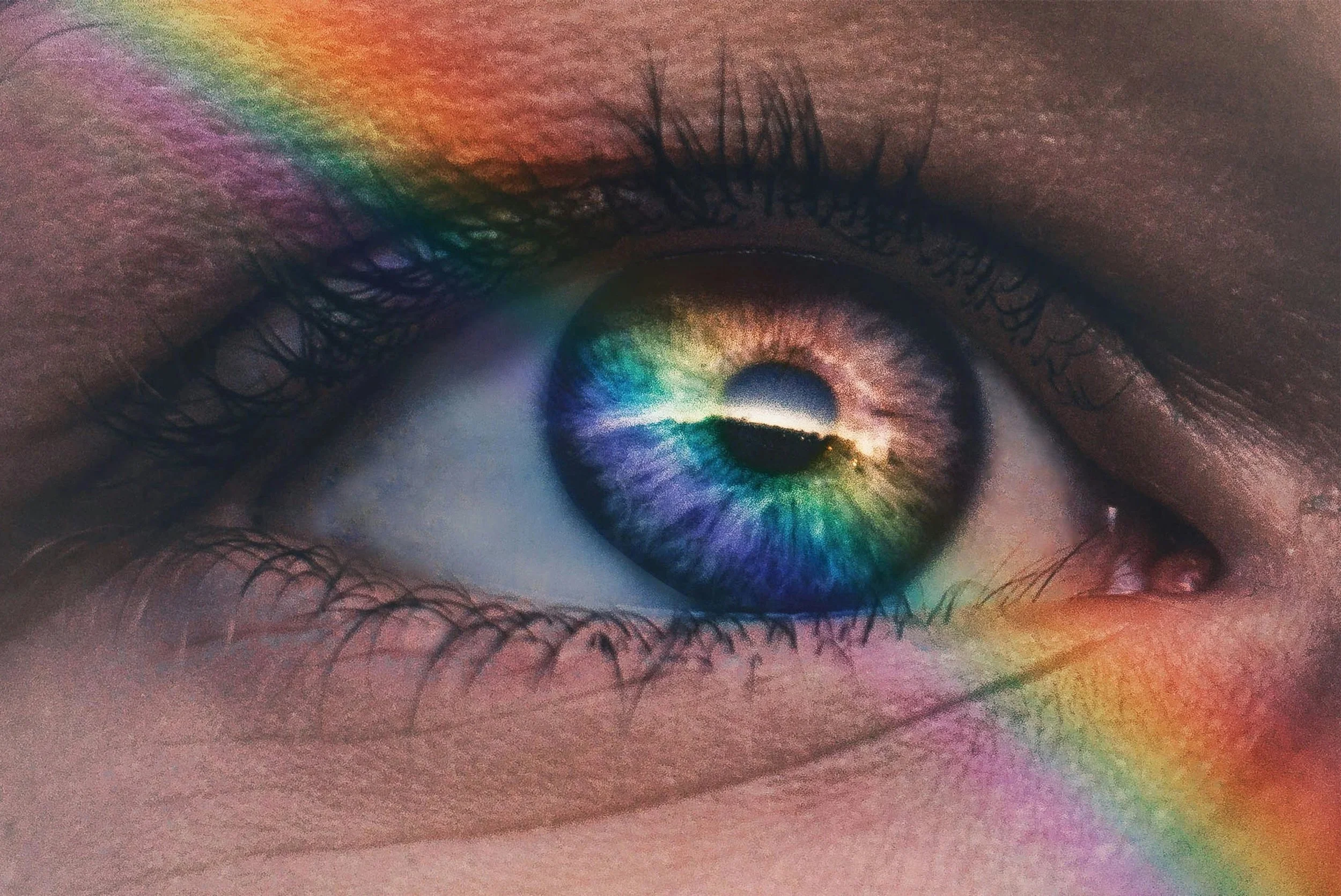 Close-up of a human eye with a rainbow reflection, showing colorful hues in the iris and a faint rainbow pattern on the skin around the eye.