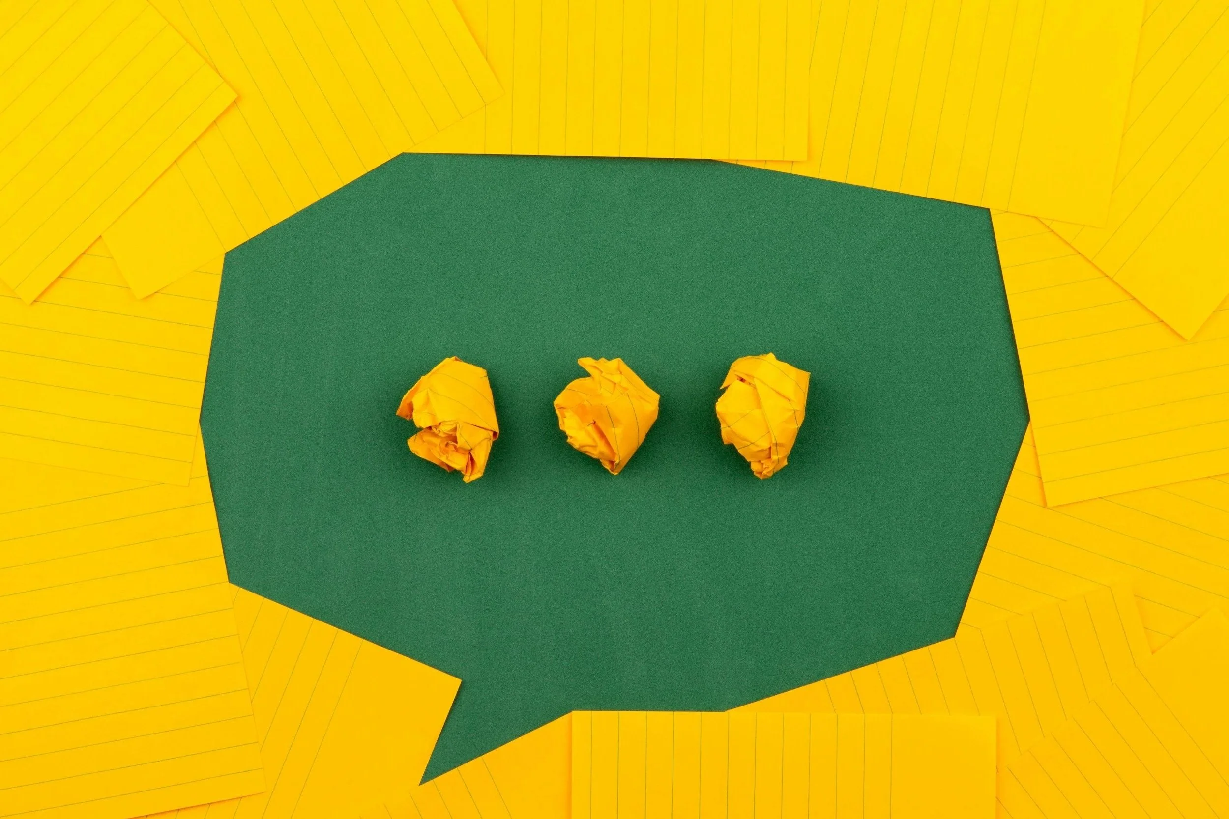 Three crumpled yellow papers inside a green speech bubble shape, surrounded by yellow paper sheets.