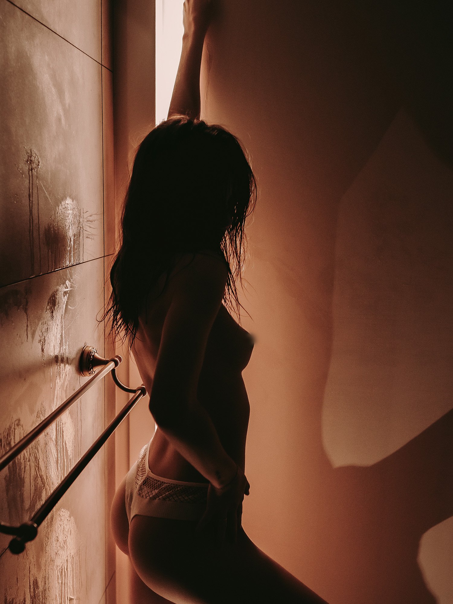 Silhouette d'une femme aux cheveux longs, debout dans une pièce sombre, avec une lumière venant par une fenêtre derrière elle.