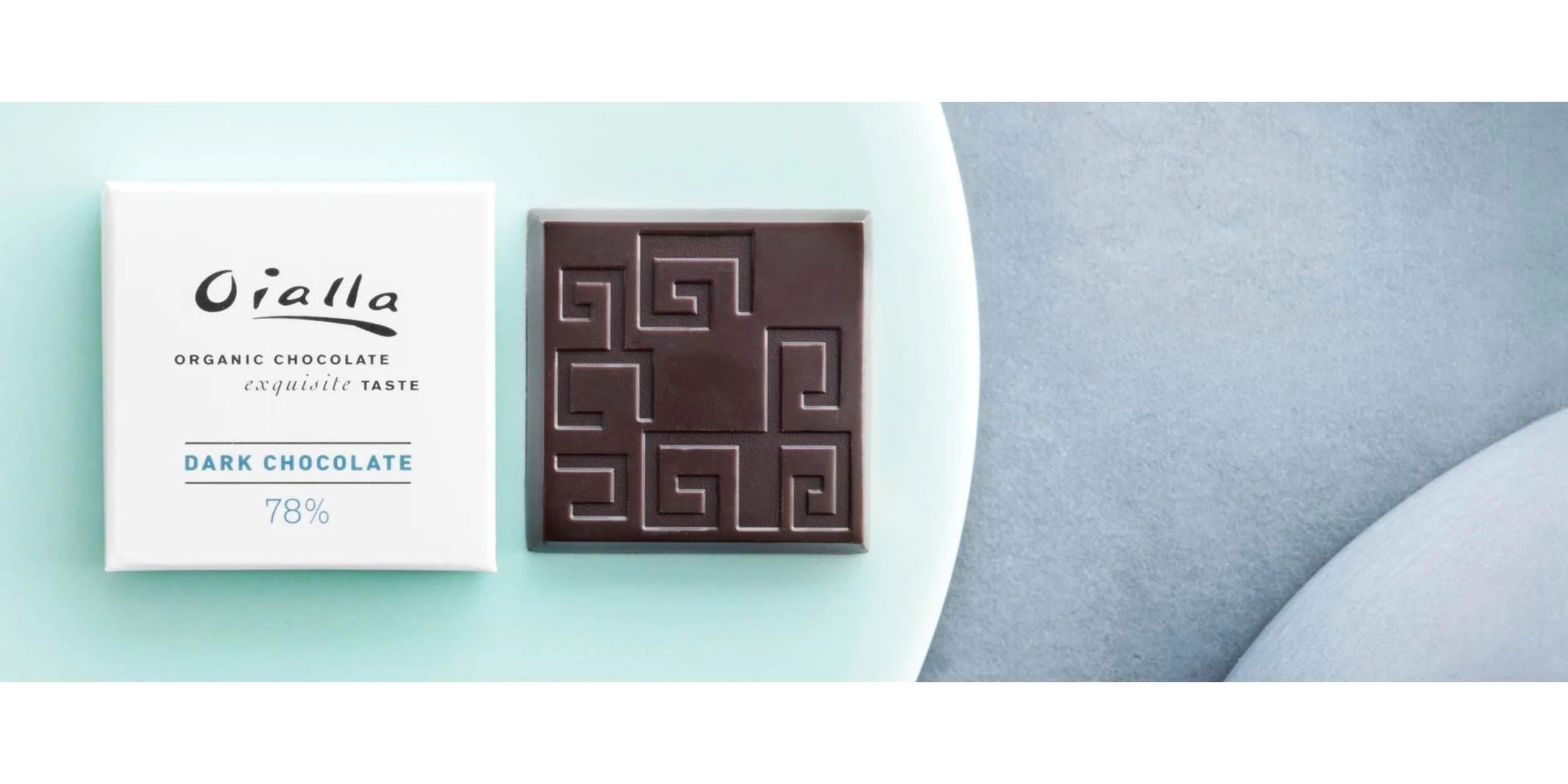 A bar of dark chocolate with geometric patterns next to a white box labeled "Oialla Organic Chocolate" and "Dark Chocolate 78%" on a pastel background.