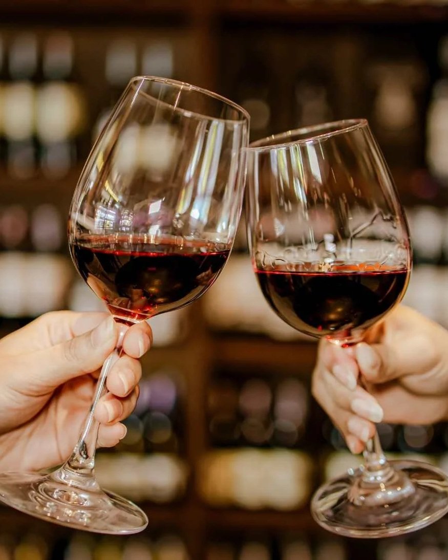 Two people clinking glasses of red wine in a bar setting.
