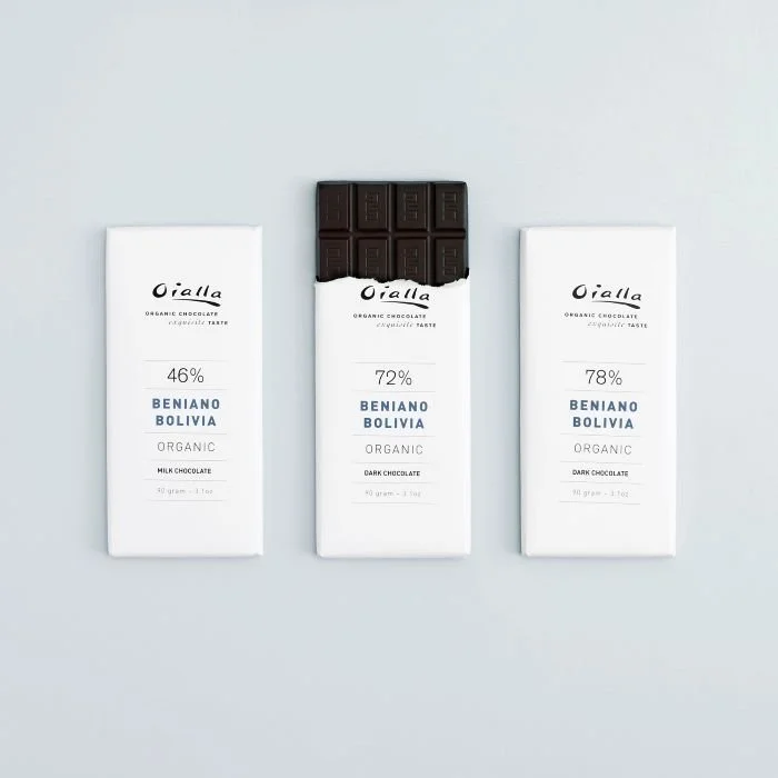 Three white chocolate bars labeled with cocoa content 46%, 72%, and 78%, from Oialla, with the 72% bar partially unwrapped and showing a piece of dark chocolate.