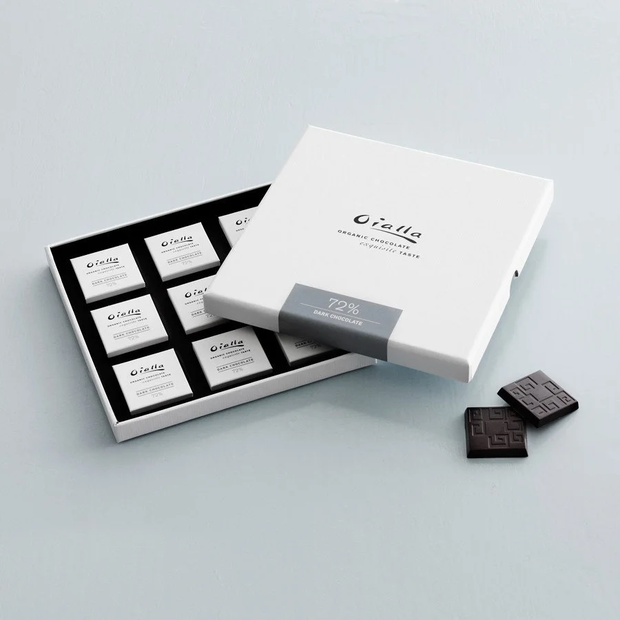 Open box of dark chocolate bars with two pieces outside the box, on a light gray surface.