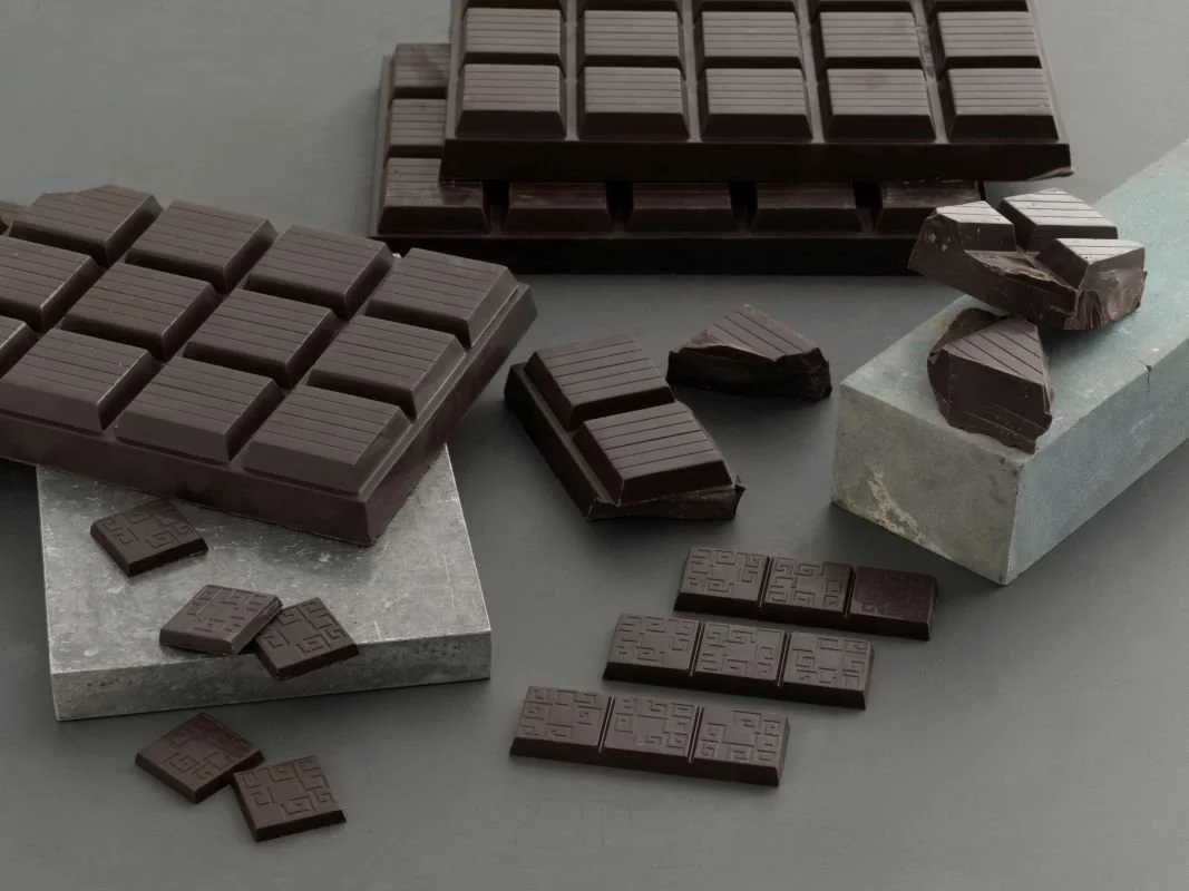 Various pieces of dark chocolate, some broken, arranged on gray surfaces and stone slabs.