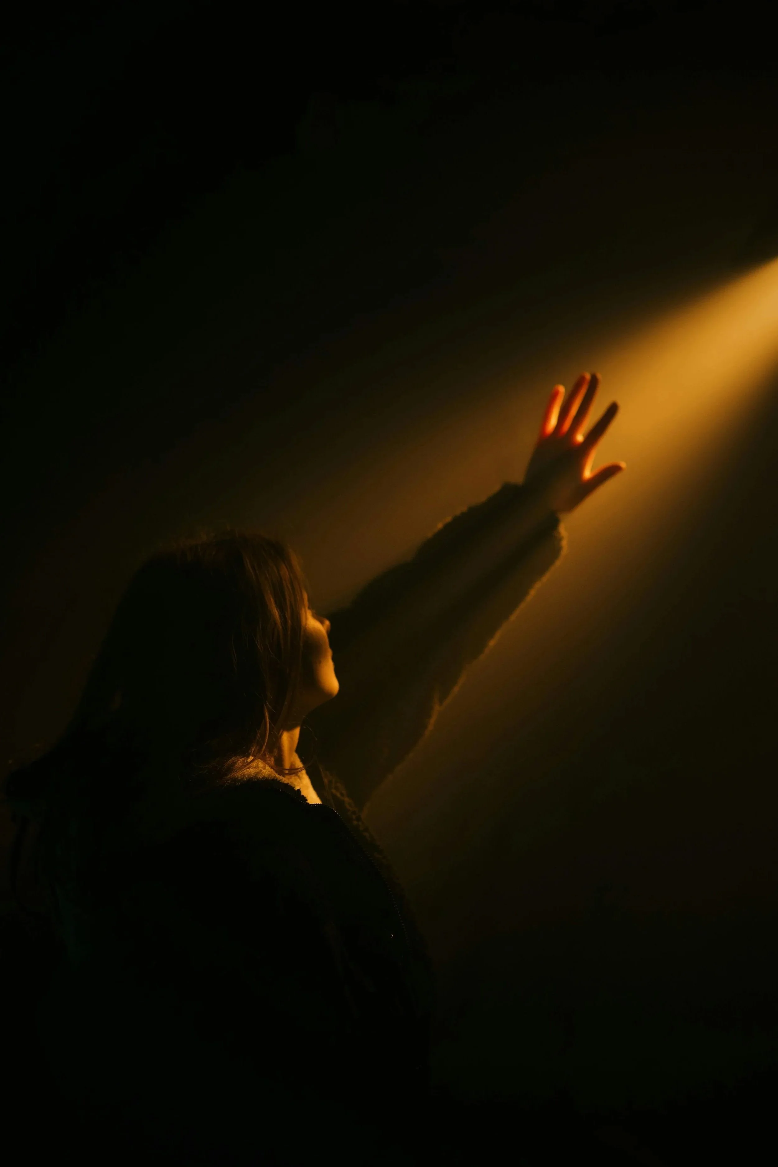 Persona con mano extendida tocando la luz dorada en un entorno oscuro.