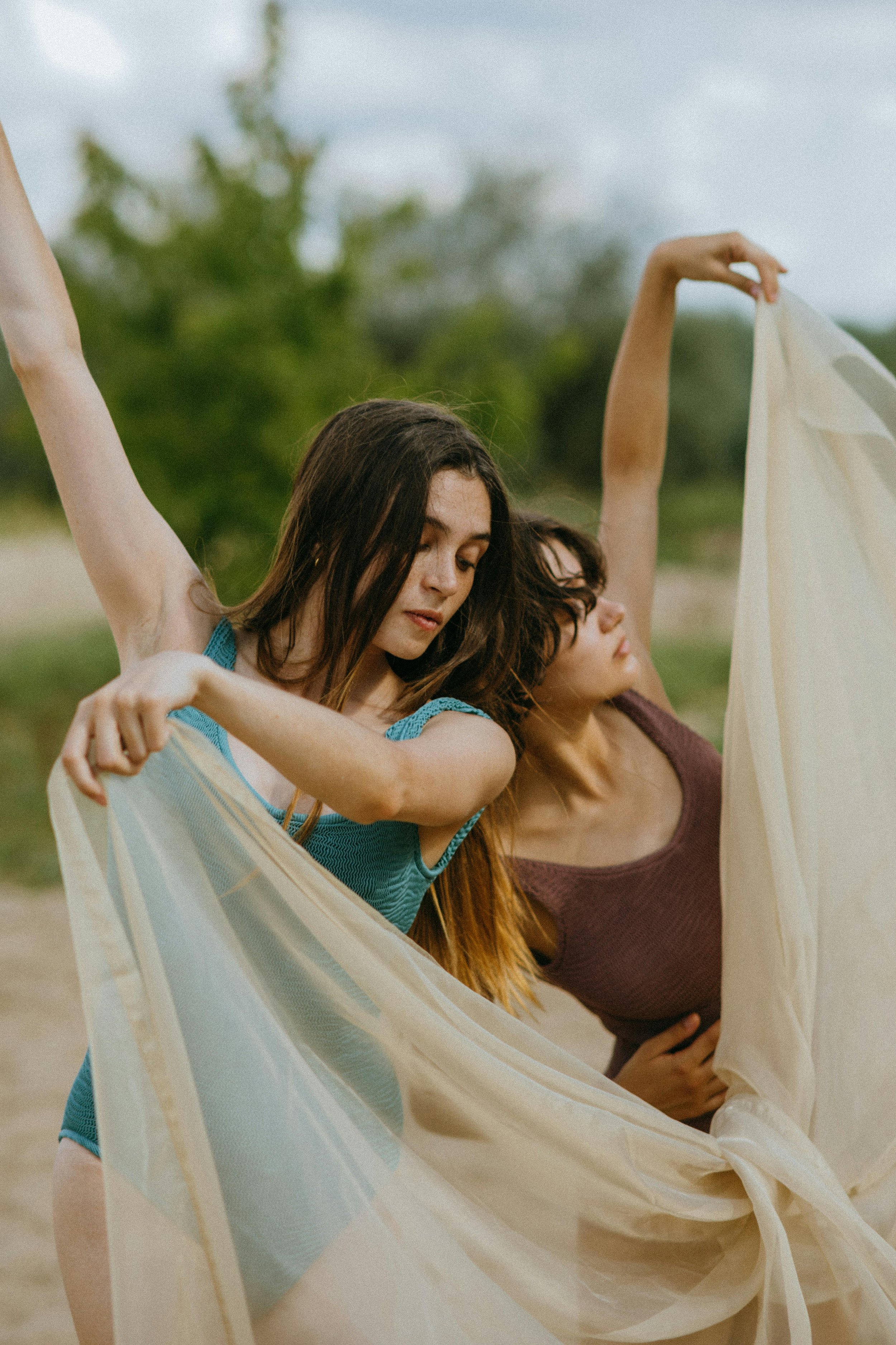 Dos jóvenes mujeres bailando con telas en un entorno natural, con árboles y cielo en el fondo.