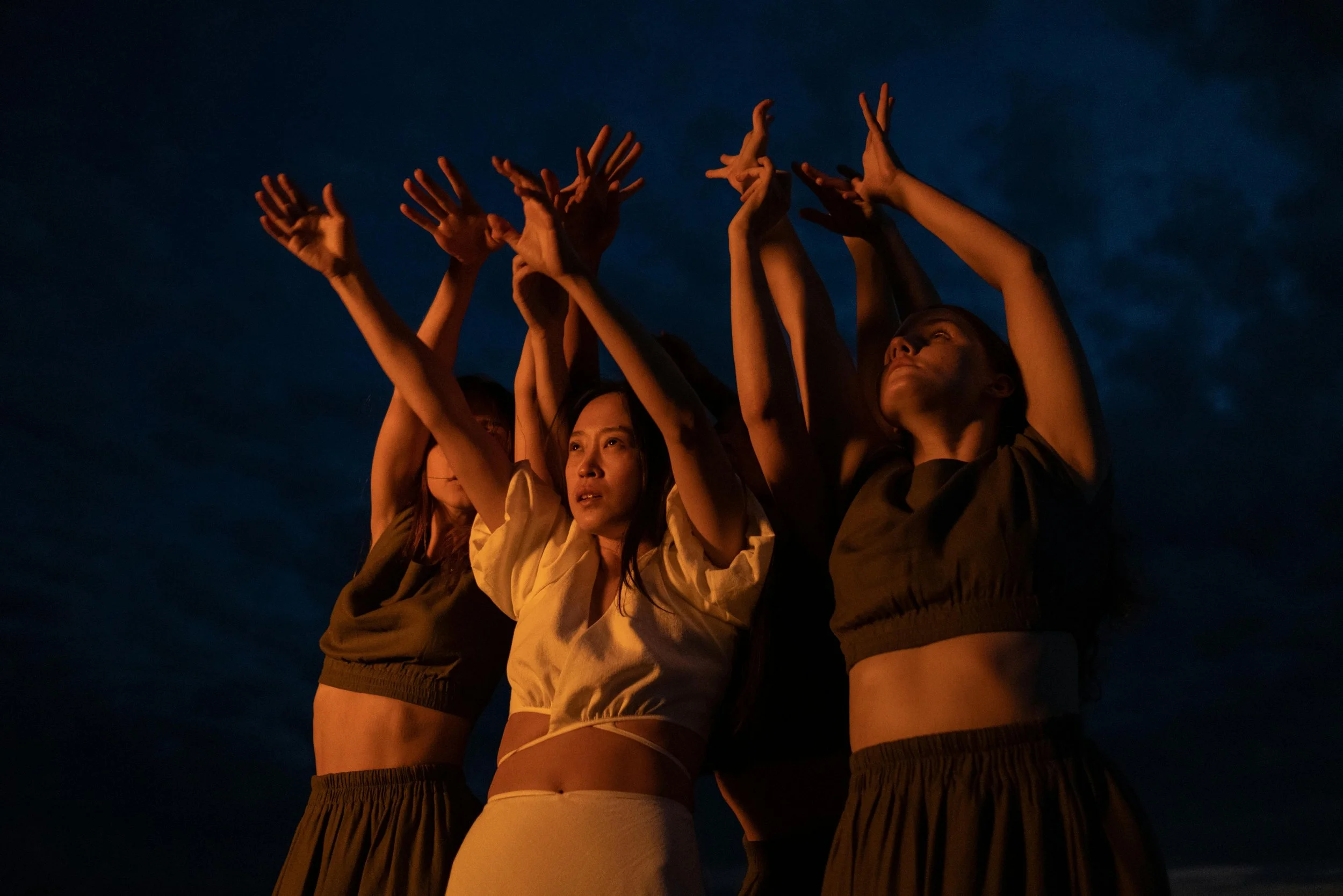Grupo de jóvenes en pose artística con brazos elevados en la noche, con cielo oscuro de fondo.