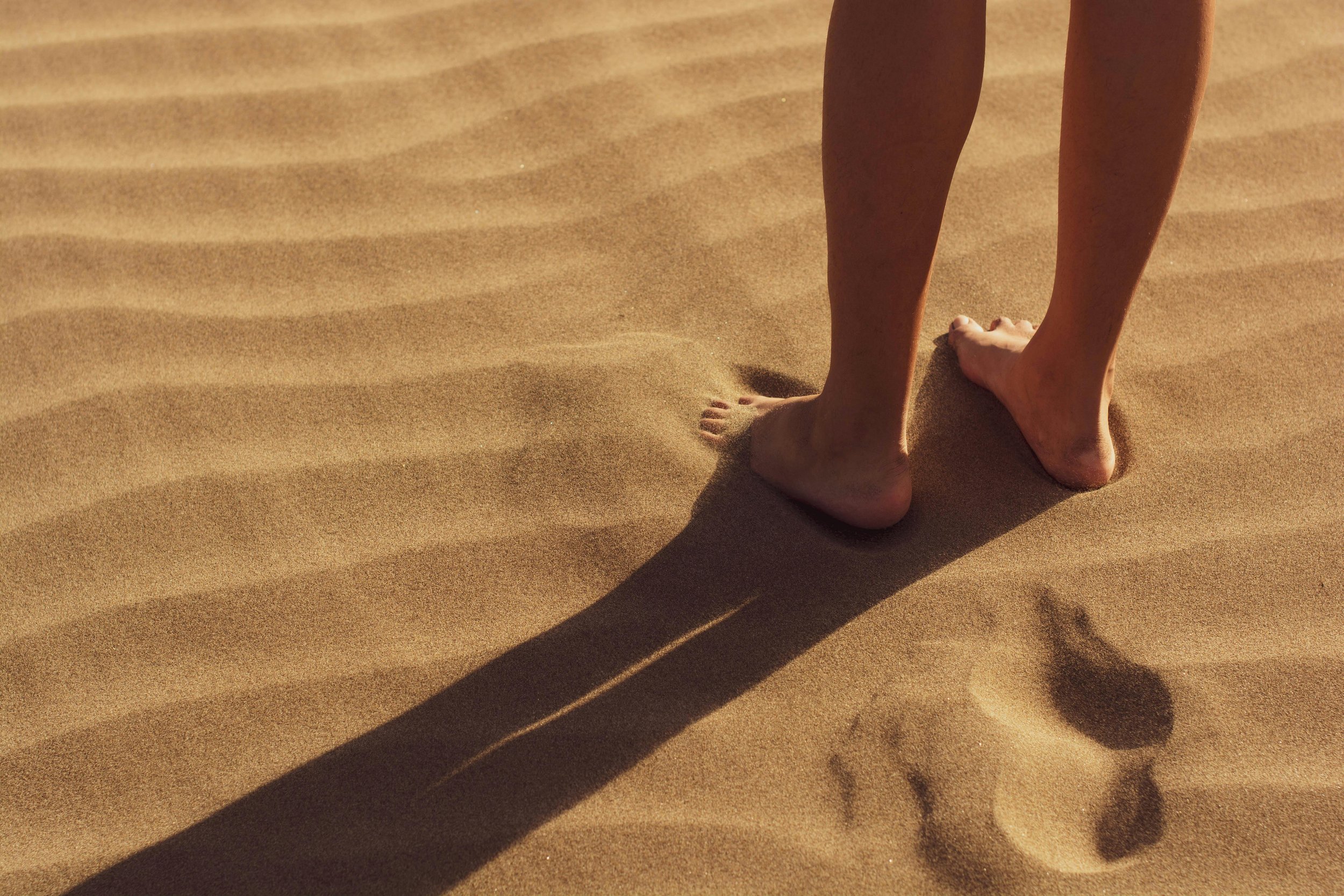 Pies y piernas de una persona caminando sobre arena en la playa durante el día.
