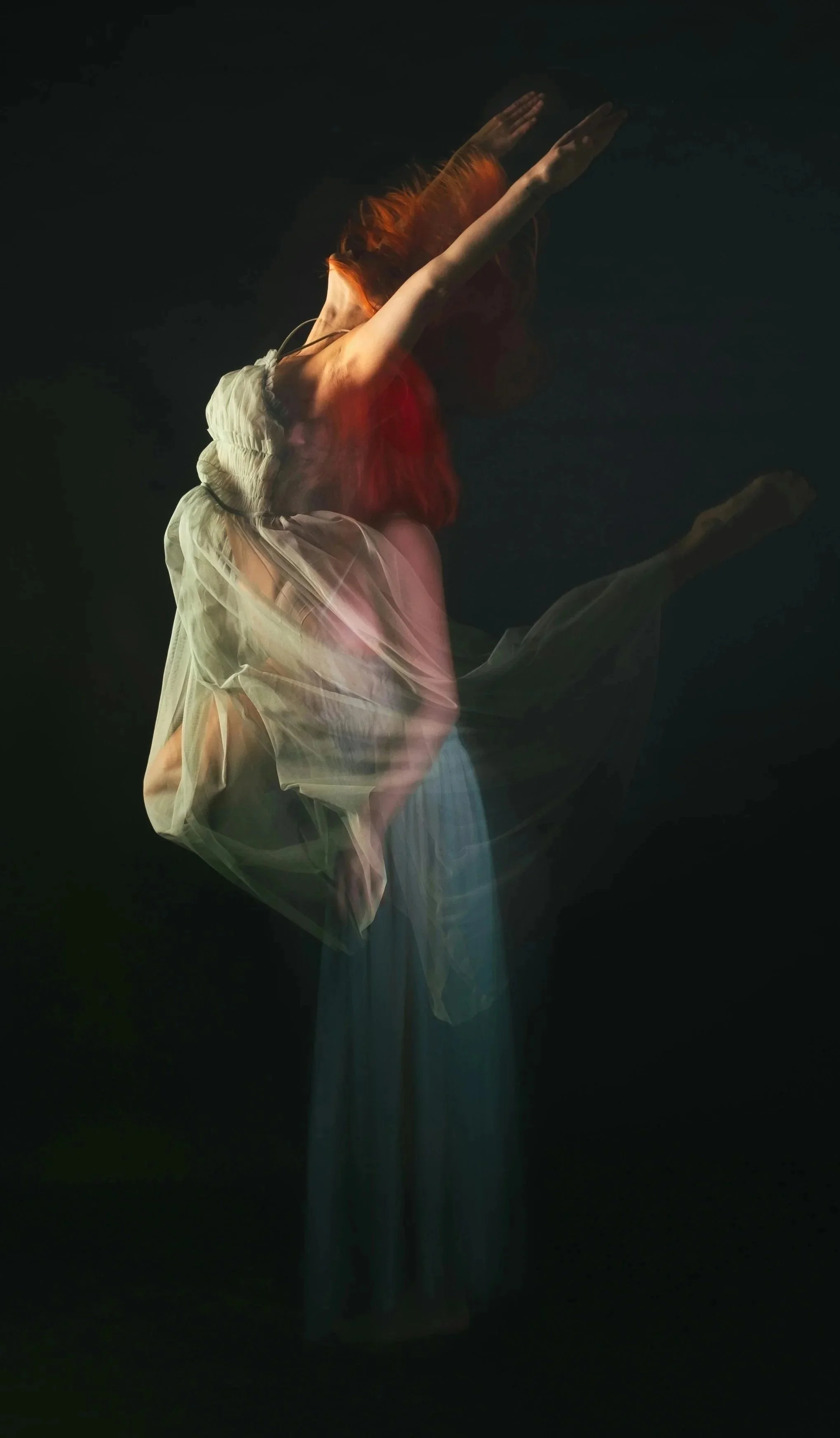 Una mujer con vestido de seda en movimiento, con cabello rizado de color rojo, en un fondo oscuro, creando un efecto de movimiento y fluidez.