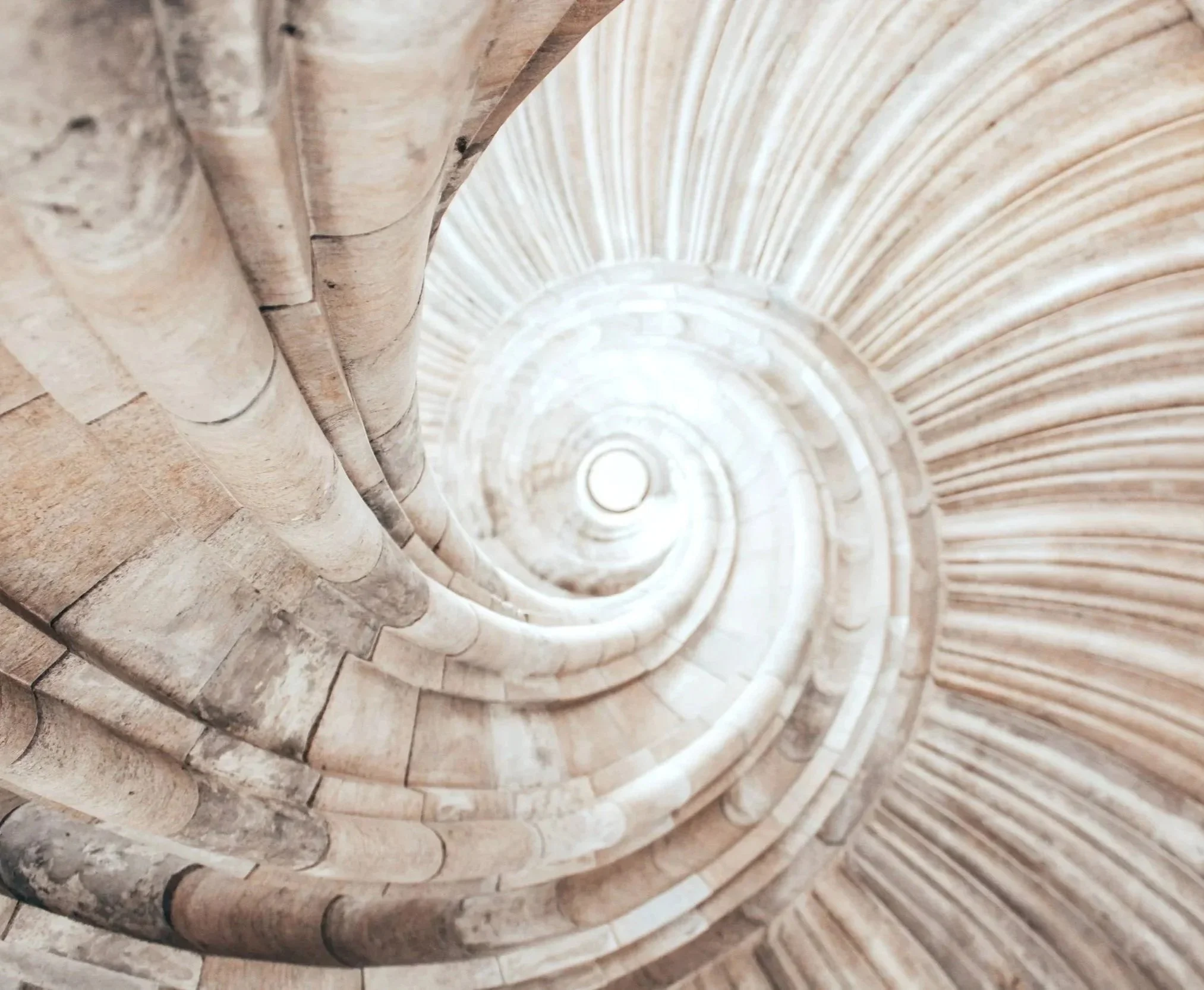 Vista desde arriba de una escalera de caracol de piedra, mostrando su estructura en espiral en un espacio cerrado.