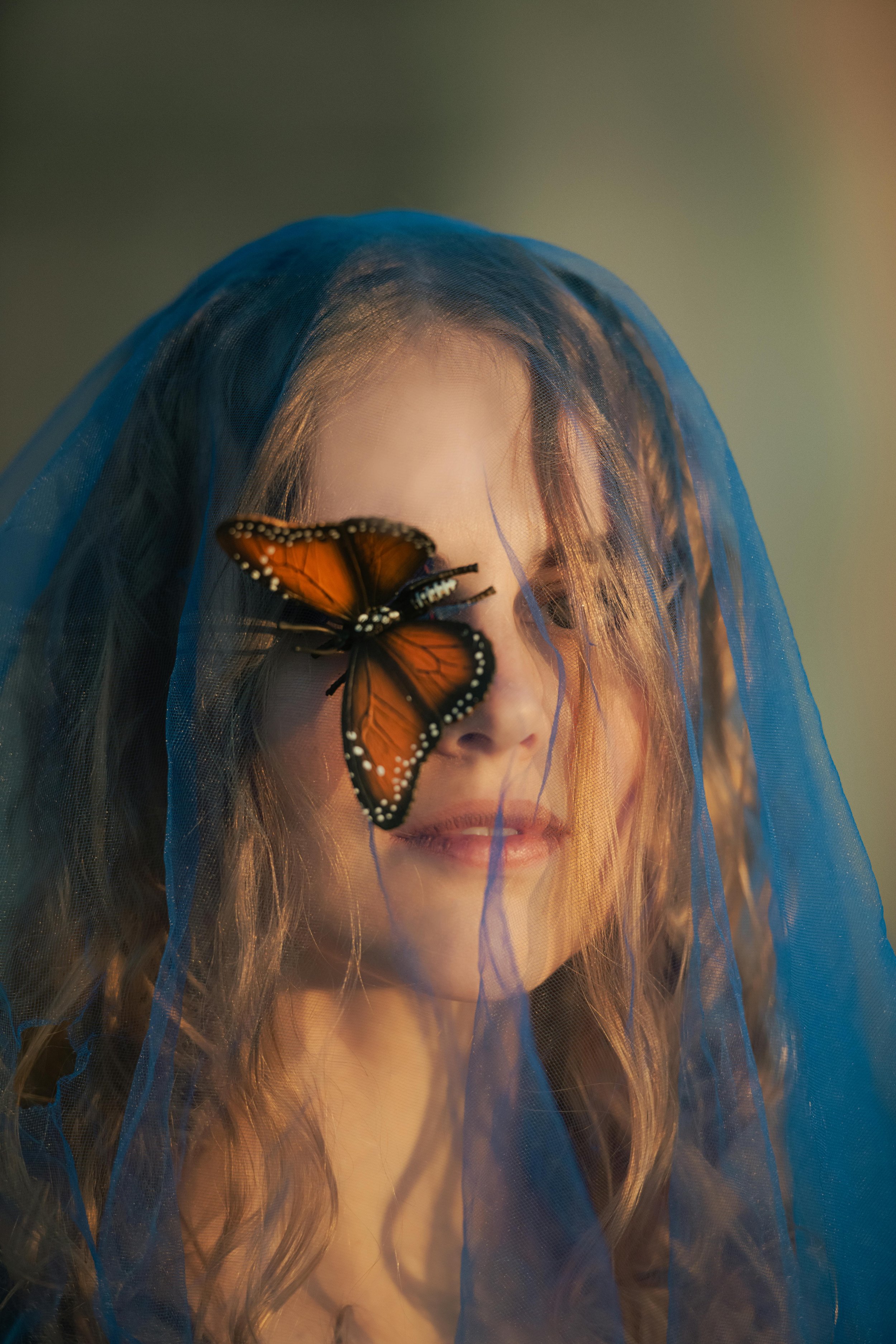 Mujer con velo azul y mariposa en la cara.