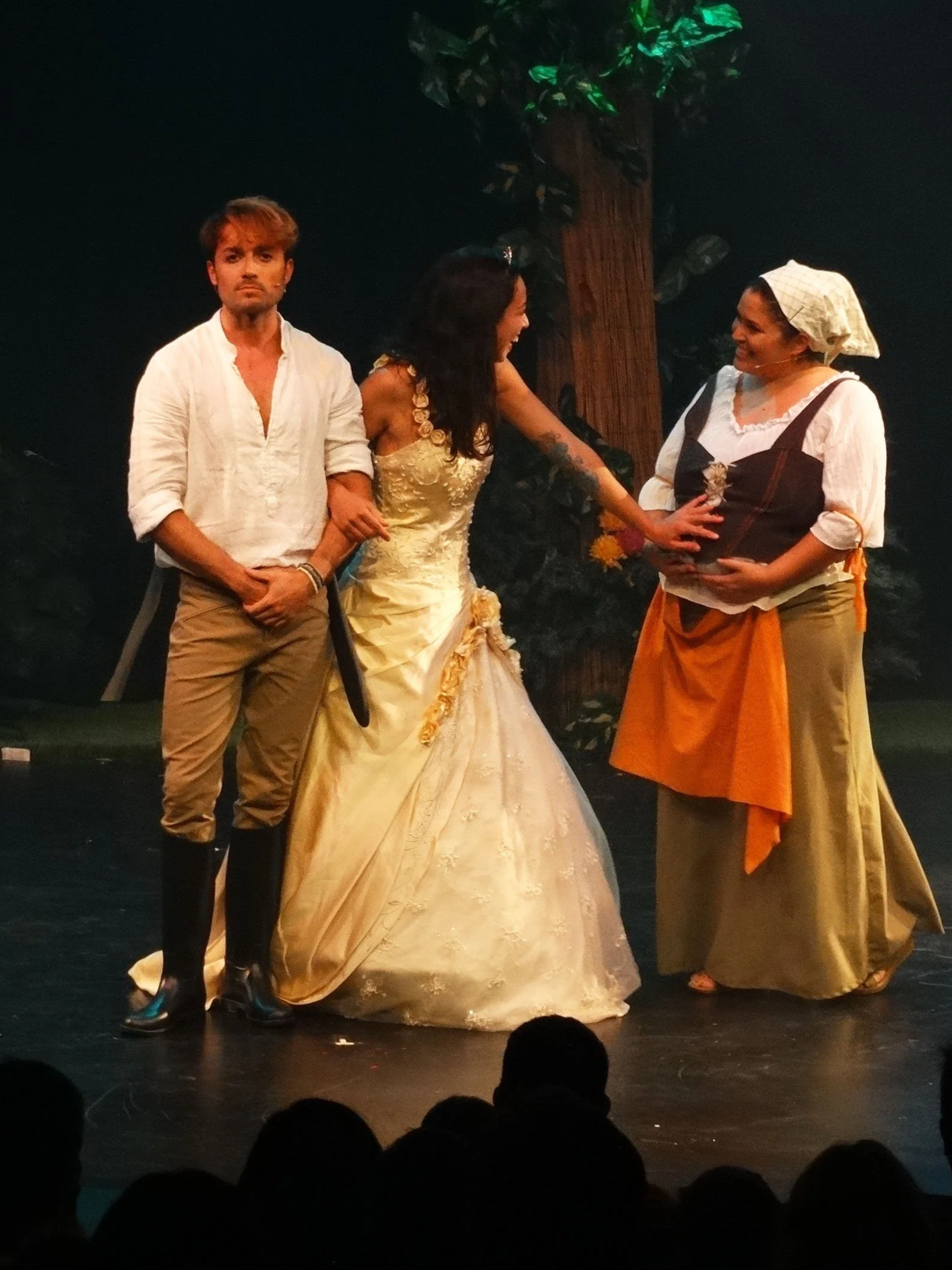 Tres actores en una obra de teatro en el escenario, representando una escena con un árbol de fondo.