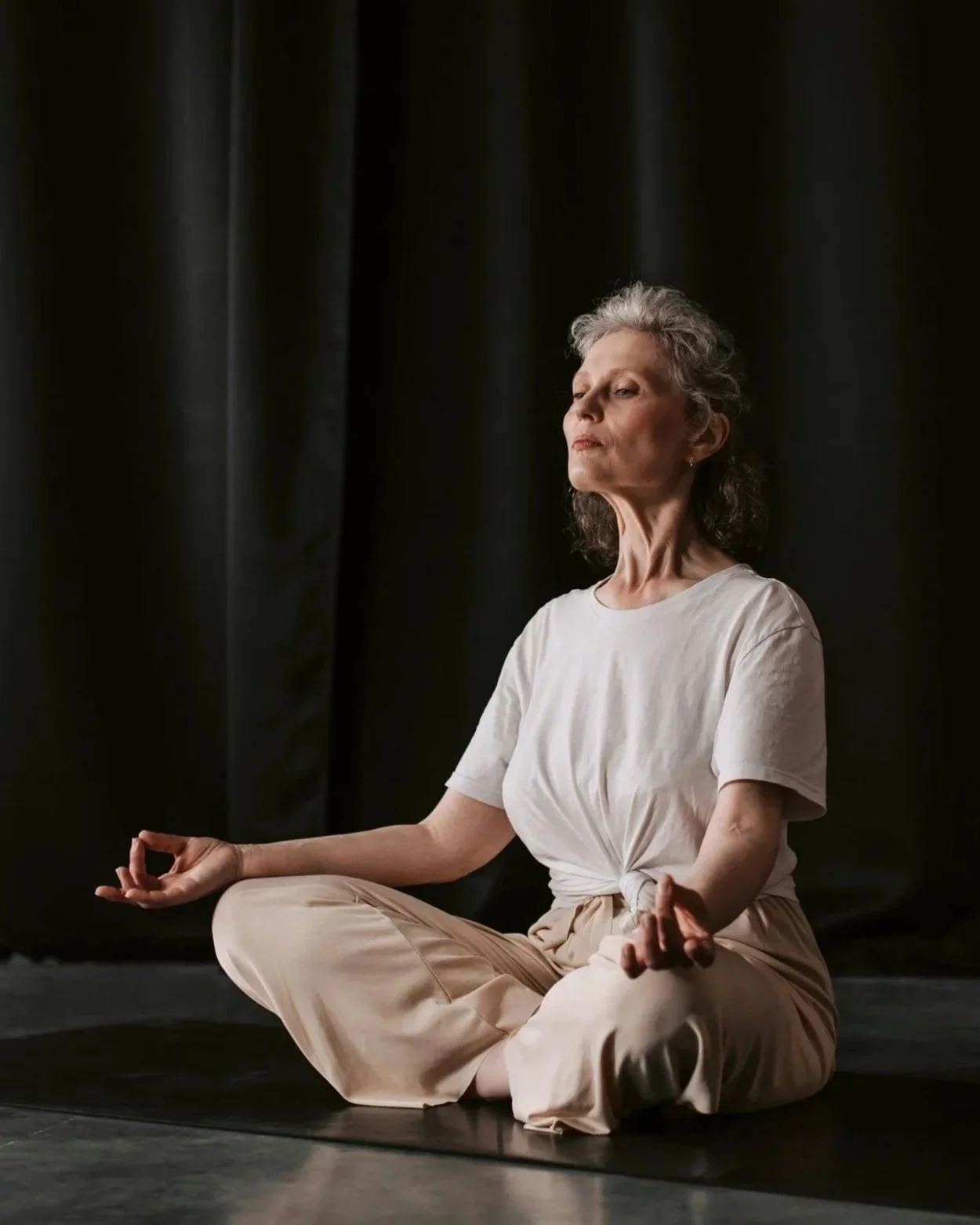 Mujer mayor practicando yoga en postura de meditación en un fondo oscuro