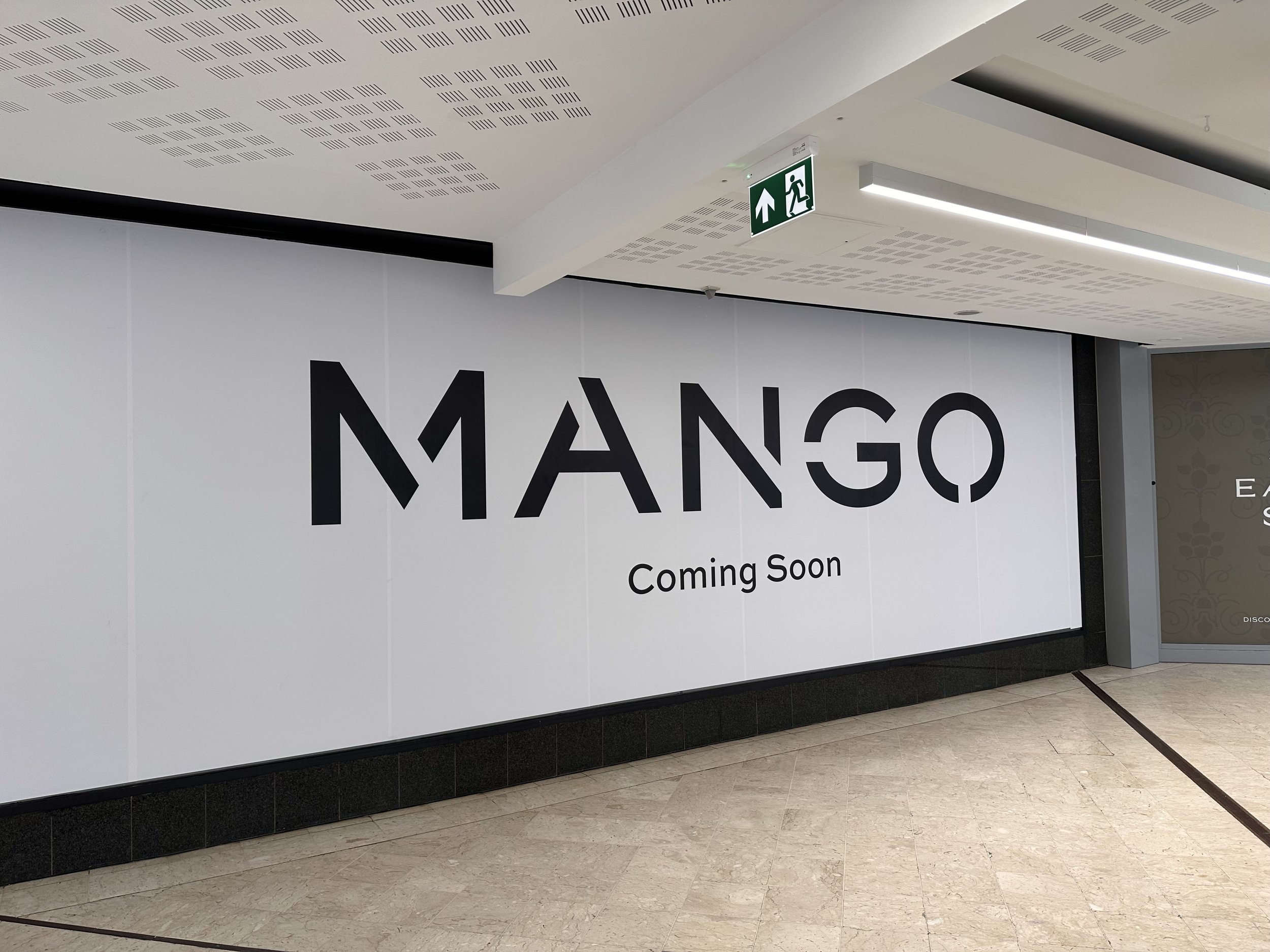 An image of a large-scale window graphic installation, depicting a large Mango logo, with text below that the store is opening soon.
