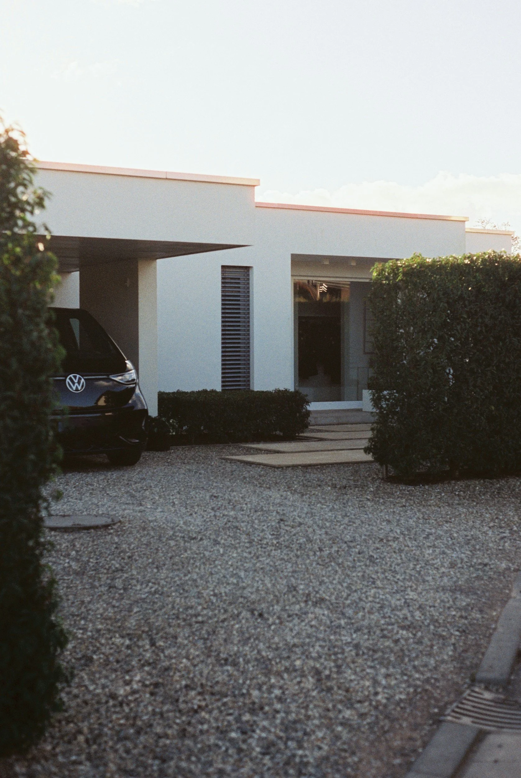 Modern house with a gravel driveway, bushes, and a parked Volkswagen EV electric car.