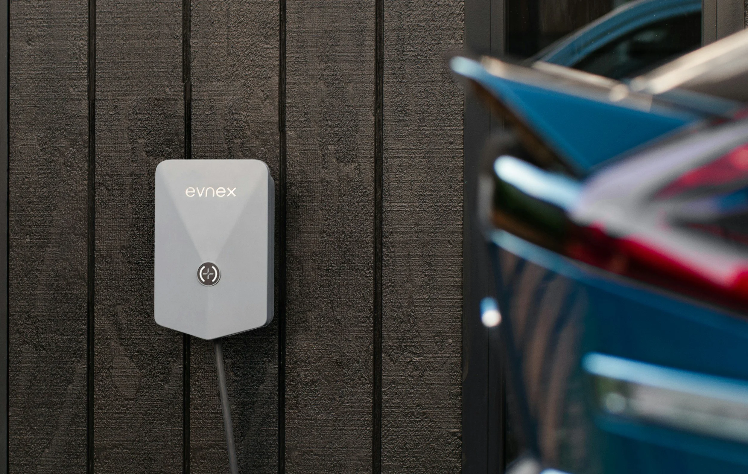 Electric vehicle charging station mounted on a dark wooden wall, with a blue car nearby.