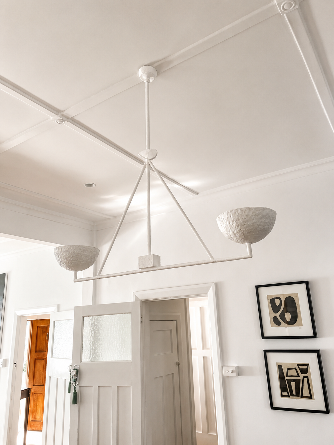 A signature handcrafted Anna Charlesworth two-bowl triangle pendant hangs from a white ceiling in a bright room of our St Kilda East project, 2026.