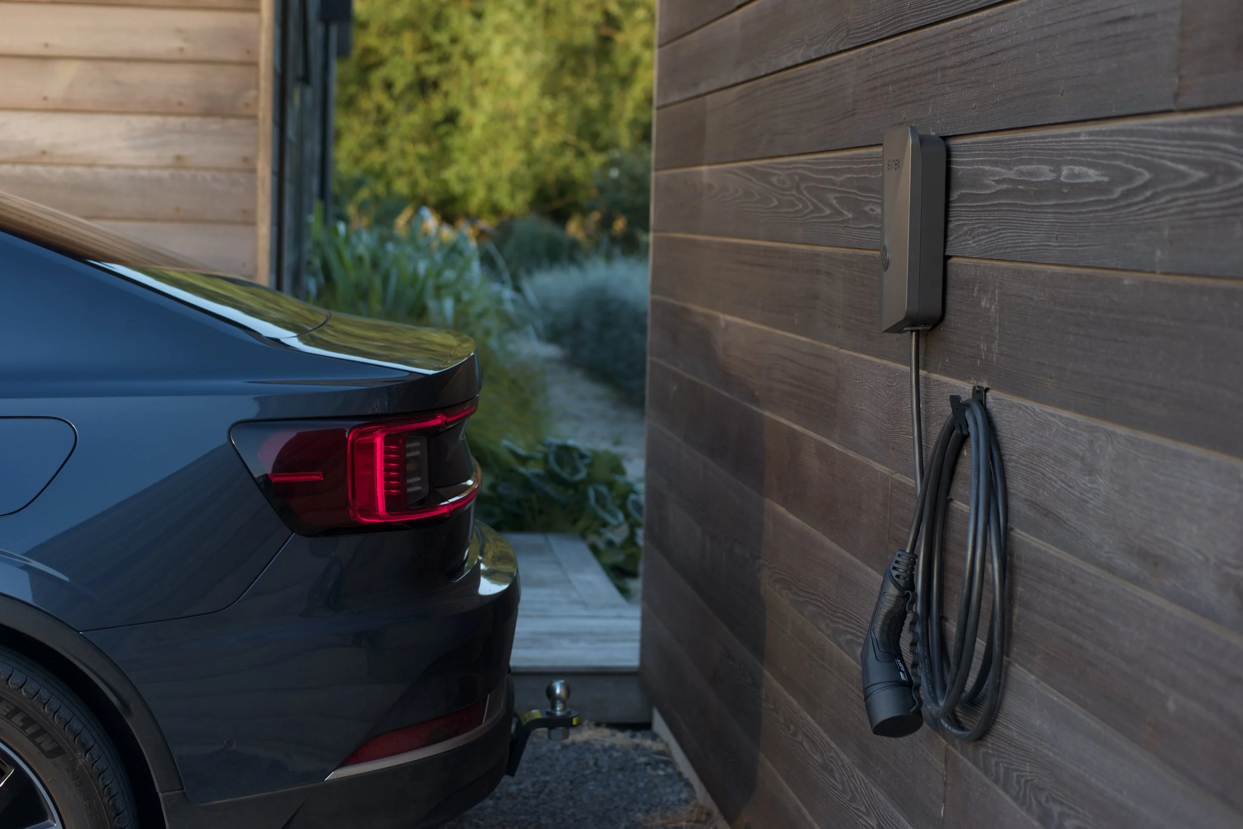 Evnex Core smart EV charger installed on exterior timber wall with electric vehicle parked in carport