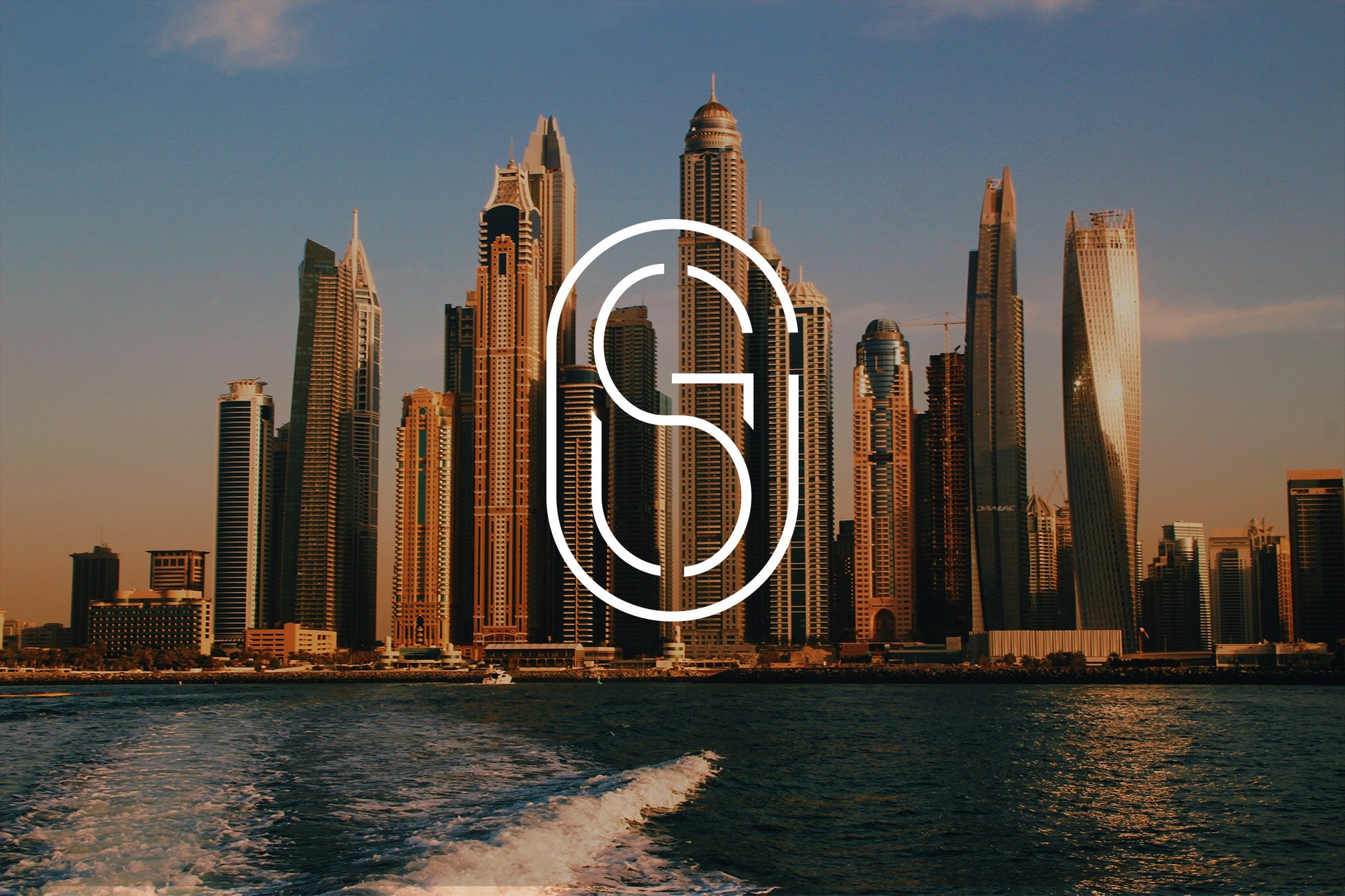 View of a city skyline with tall modern skyscrapers during sunset, water in the foreground with boat wake.