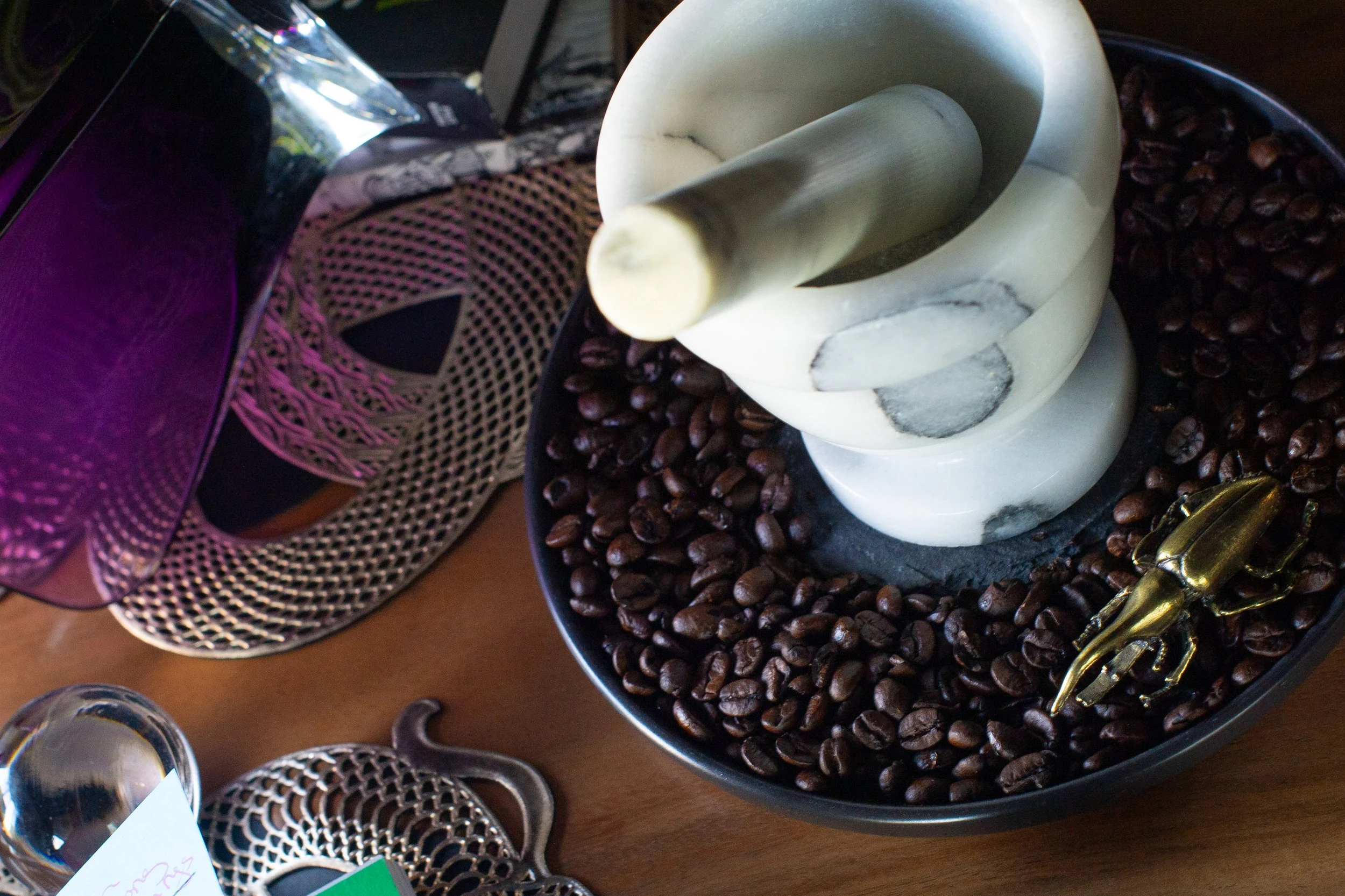 A green and white marble mortar and pestle surrounded by coffee beans on a black plate.